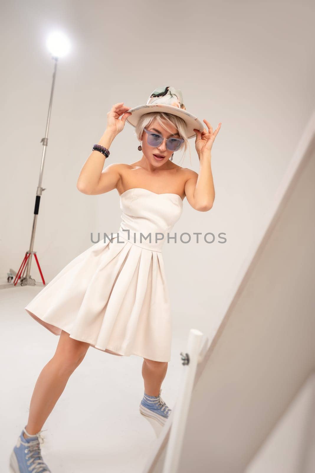 A naughty fashionable girl in a dress is fooling around and dancing in front of a mirror in a studio with a white background copy paste