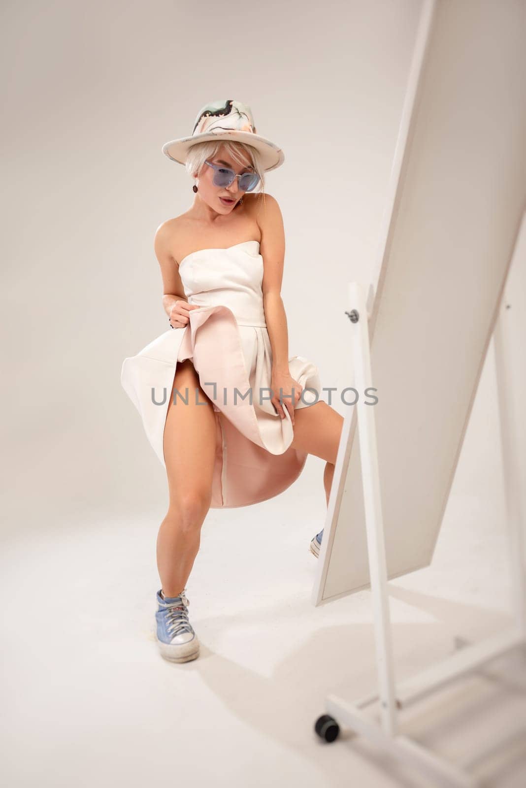 A naughty fashionable girl in a dress is fooling around and dancing in front of a mirror in a studio with a white background copy paste by Rotozey