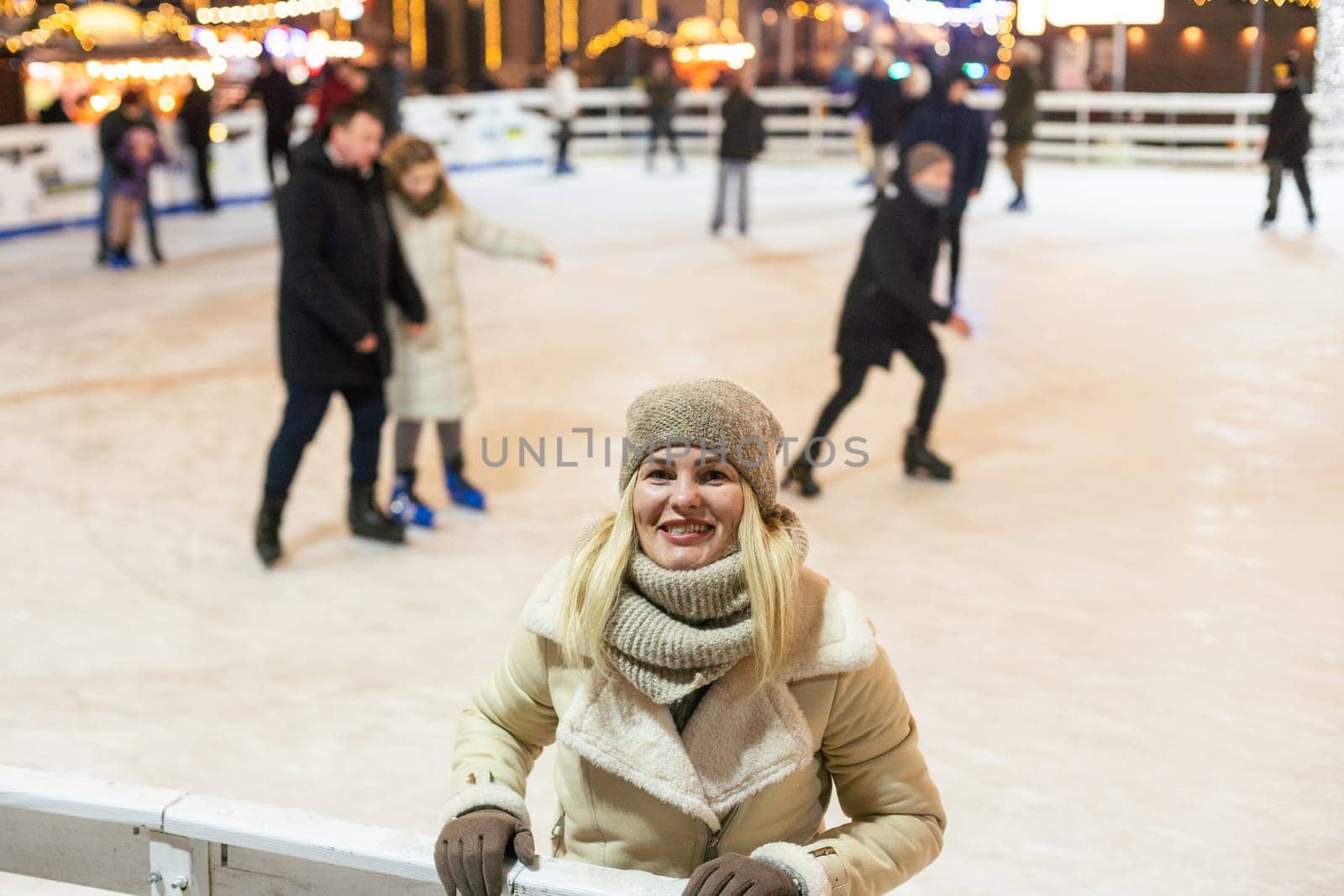 Young woman ice skating on the ice arena in the city square in winter on Christmas Eve. Winter holiday. New Year magic. Lights around. High quality photo