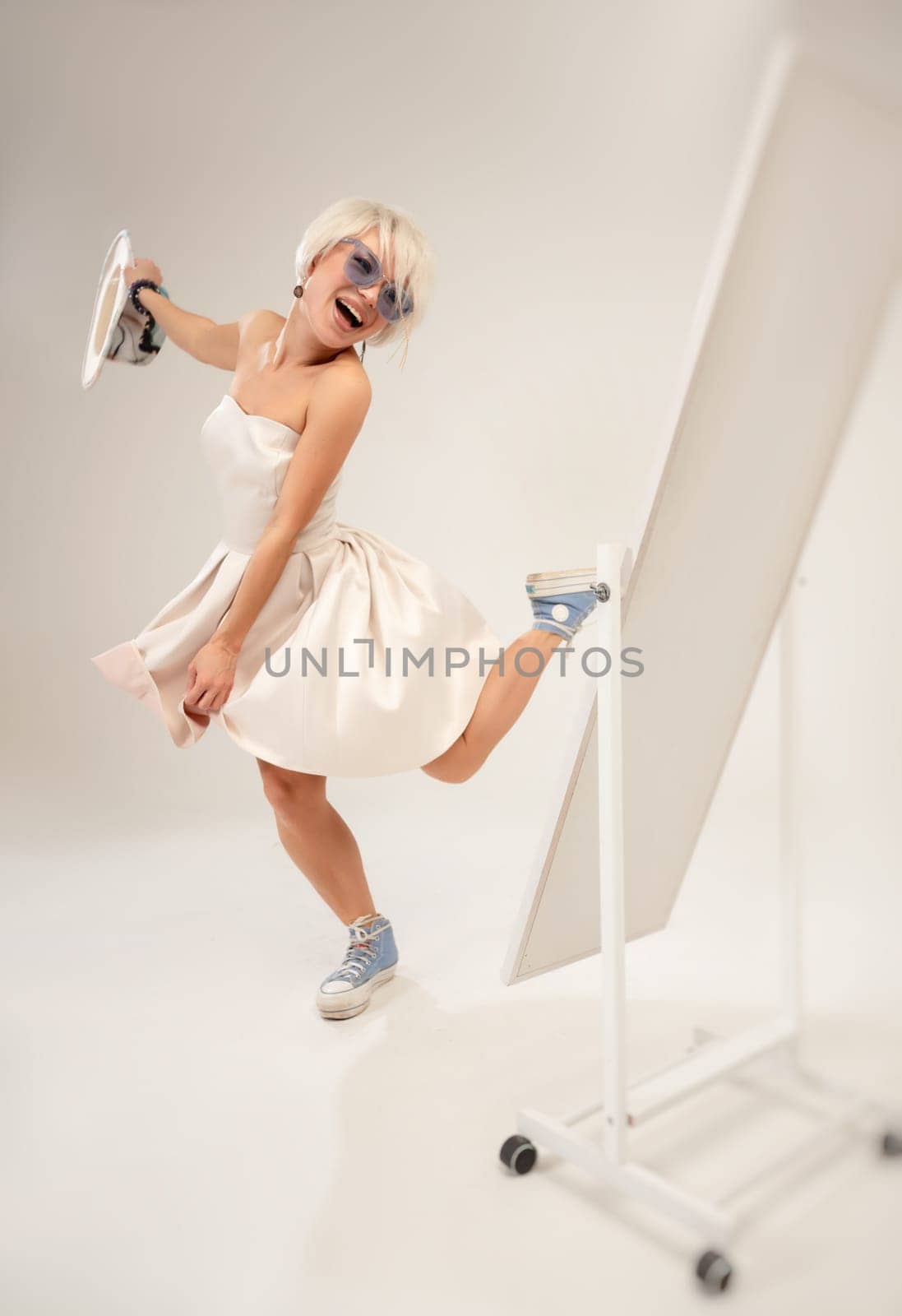 A naughty fashionable girl in a dress is fooling around and dancing in front of a mirror in a studio with a white background copy paste by Rotozey
