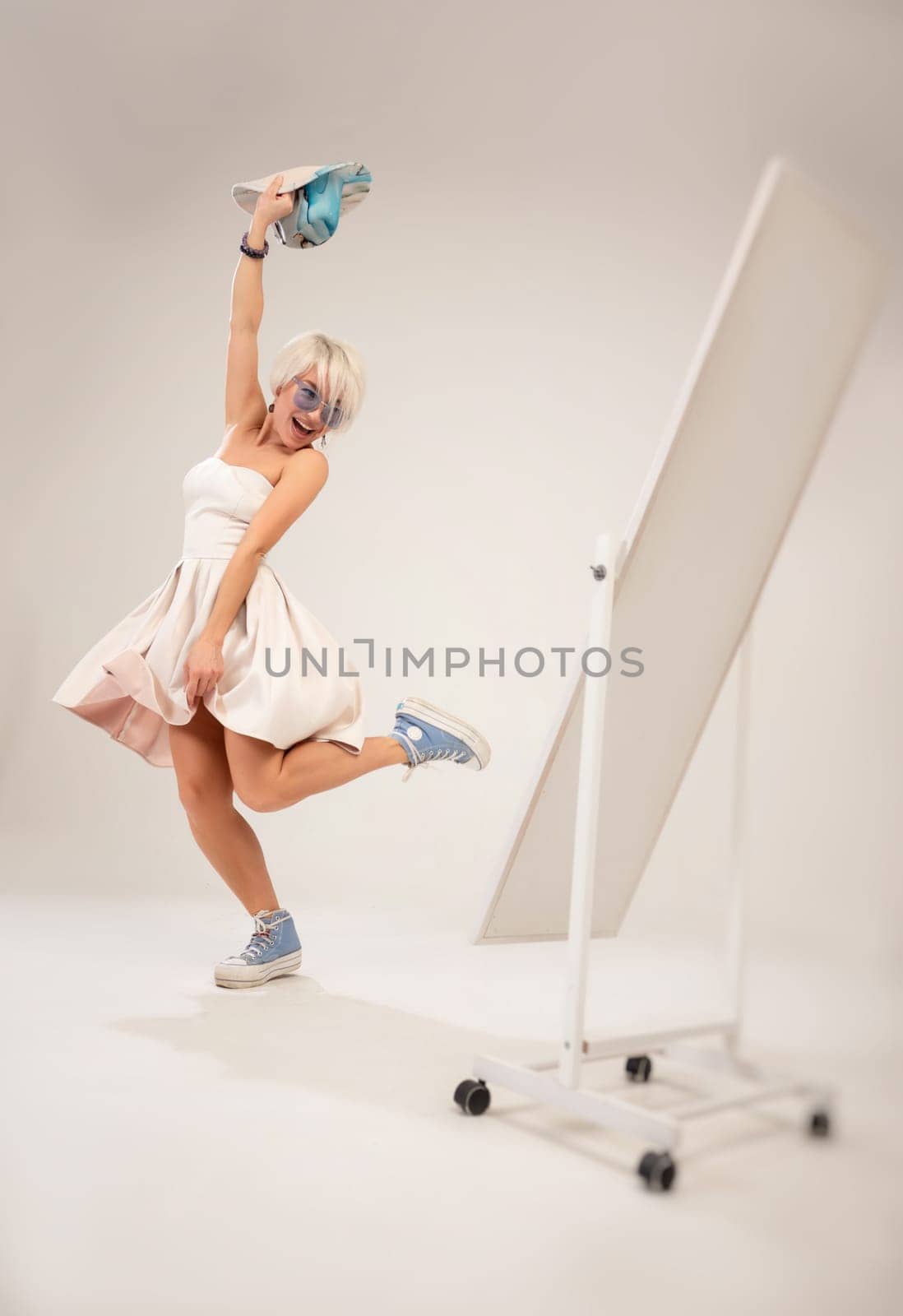 A naughty fashionable girl in a dress is fooling around and dancing in front of a mirror in a studio with a white background copy paste