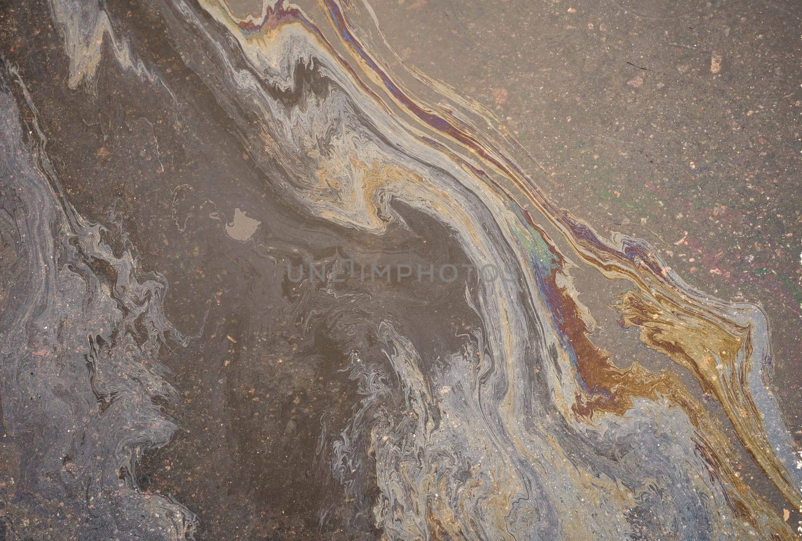 Rainbow-colored oil floating on water after rain on asphalt. Gasoline stains. Colored texture, natural background.