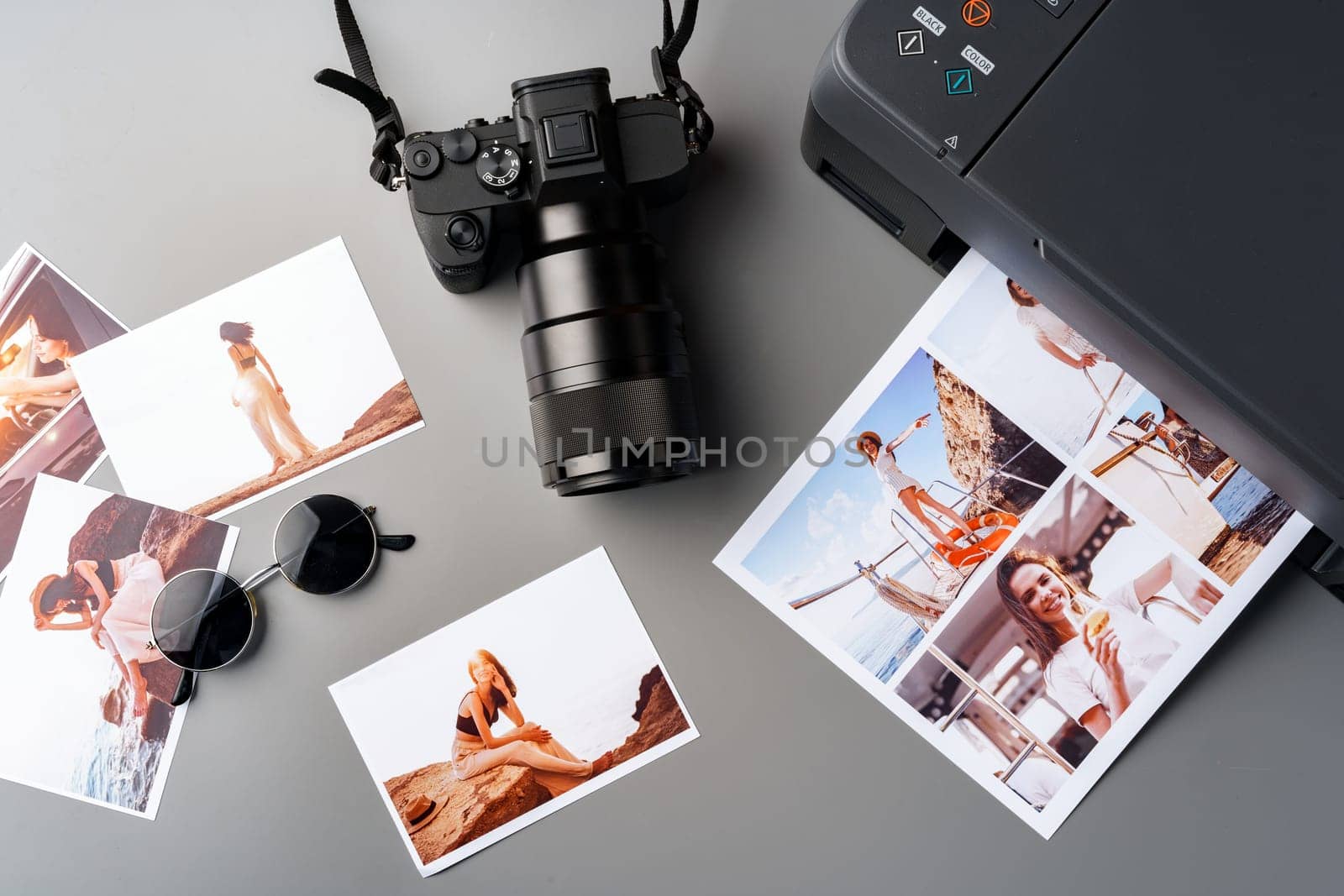Photo camera with colorful printer photos on gray desk close up