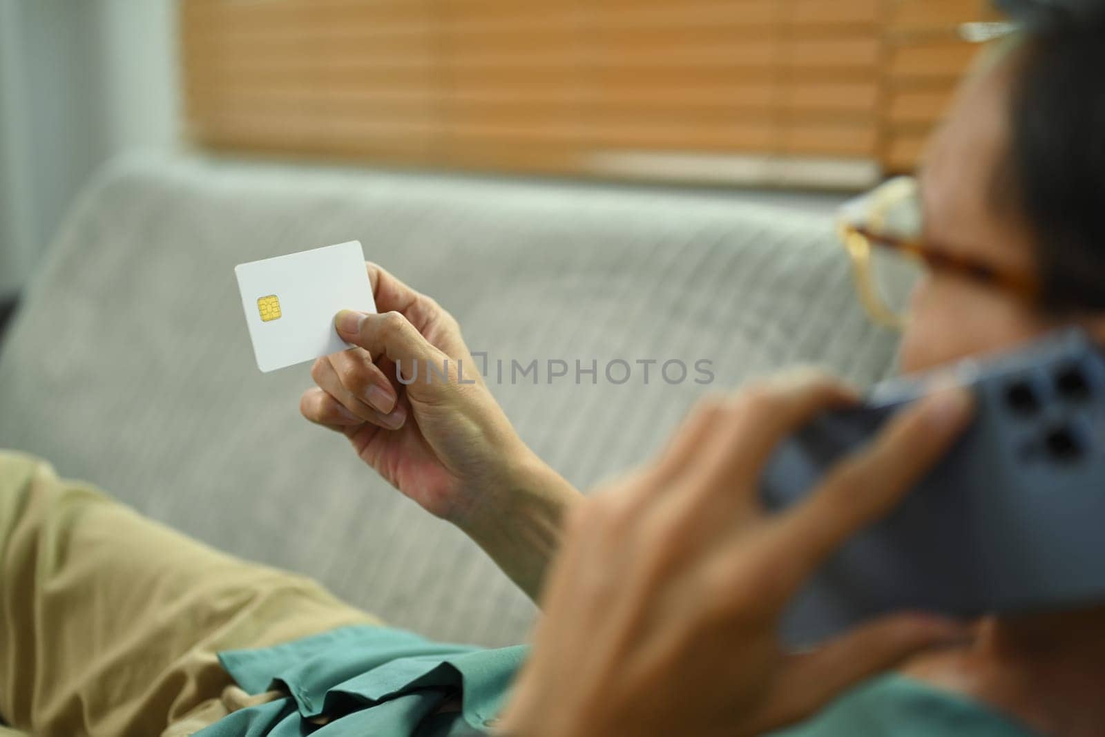 Senior man holding credit card and talking on mobile phone with conversation with customer service representative