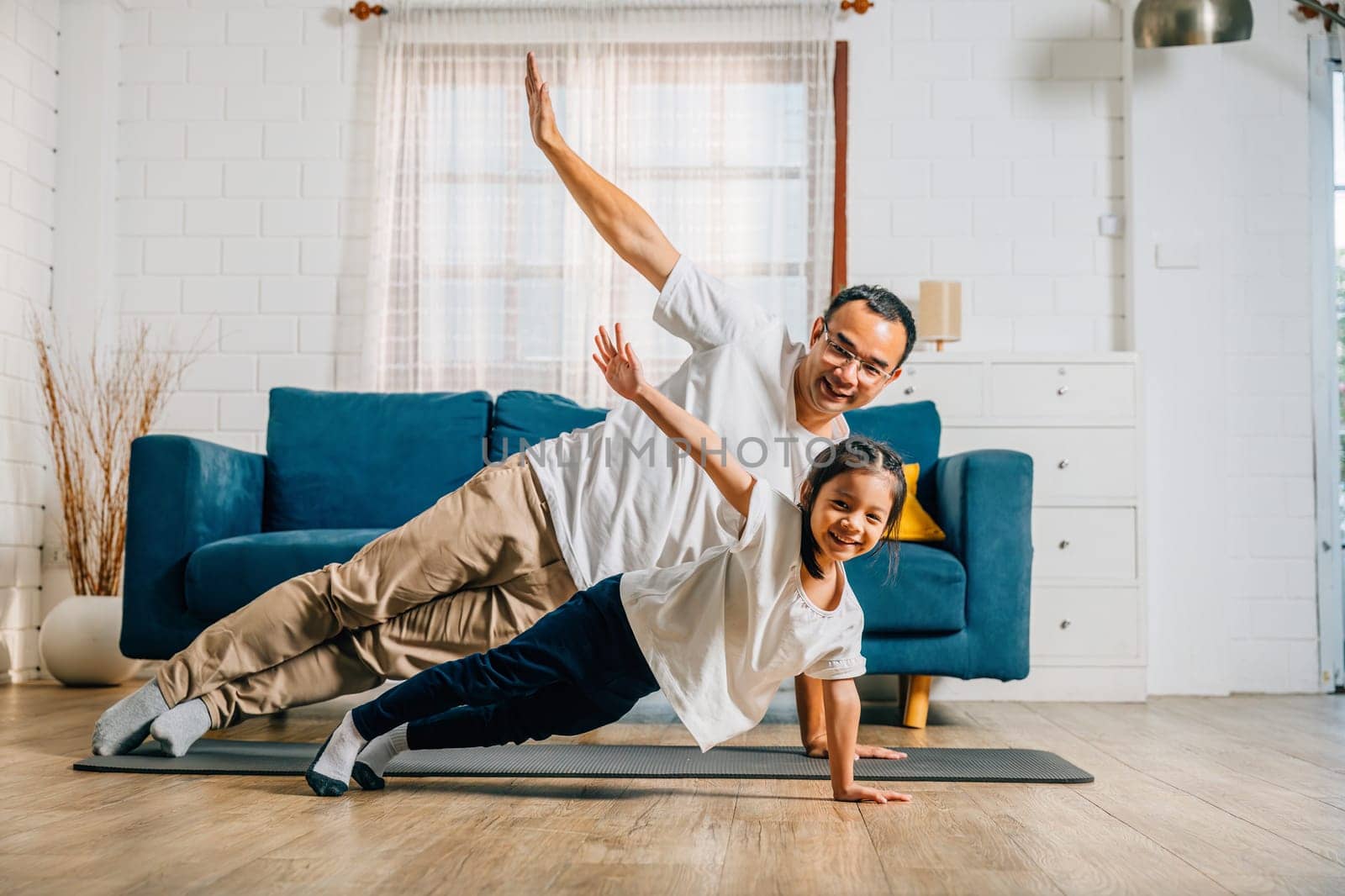 A father and his daughter find joy in yoga at home practicing togetherness happiness by Sorapop