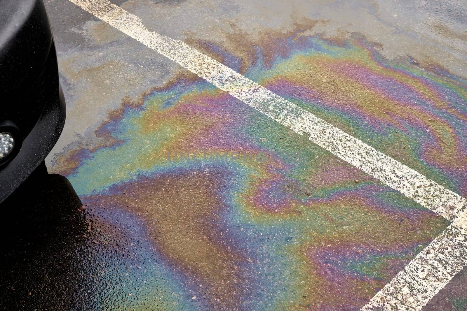 Colorful gas stain on wet asphalt. Oil stain or gasoline caused by a leak under a car. Environmental pollution concept.