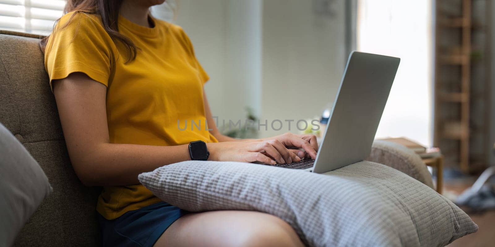 Young woman Asian using laptop pc computer on couch relax surfing the internet at home. lifestyle relaxation concept by nateemee