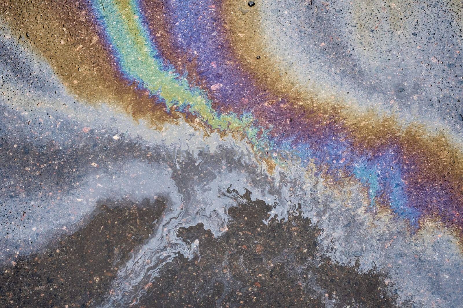 Petroleum fuel spilled on wet asphalt, abstract background.