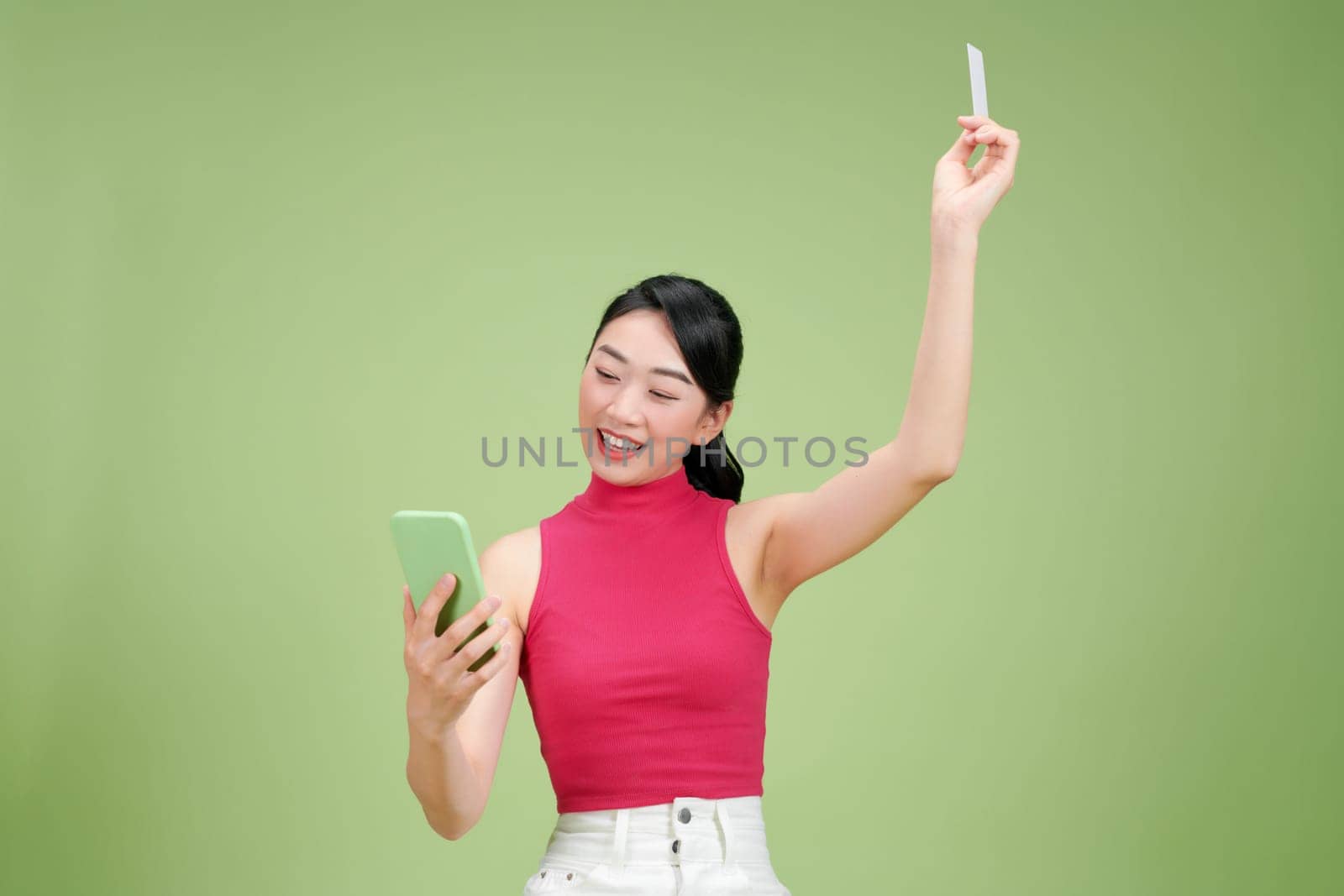 Smiling woman sitting on podium showing credit card and holding smartphone in another hand by makidotvn