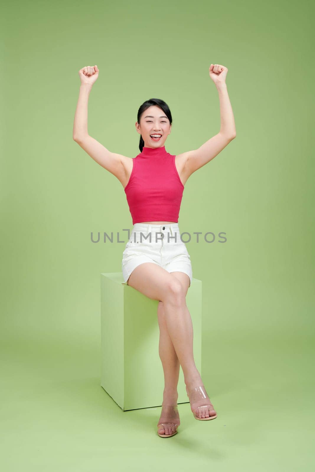 Young charming lady sitting podium raised arms fists up astonished realize luck on green background