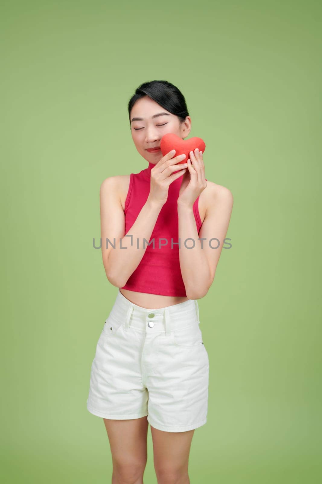 Love and valentines day woman holding heart smiling cute and adorable isolated on green background