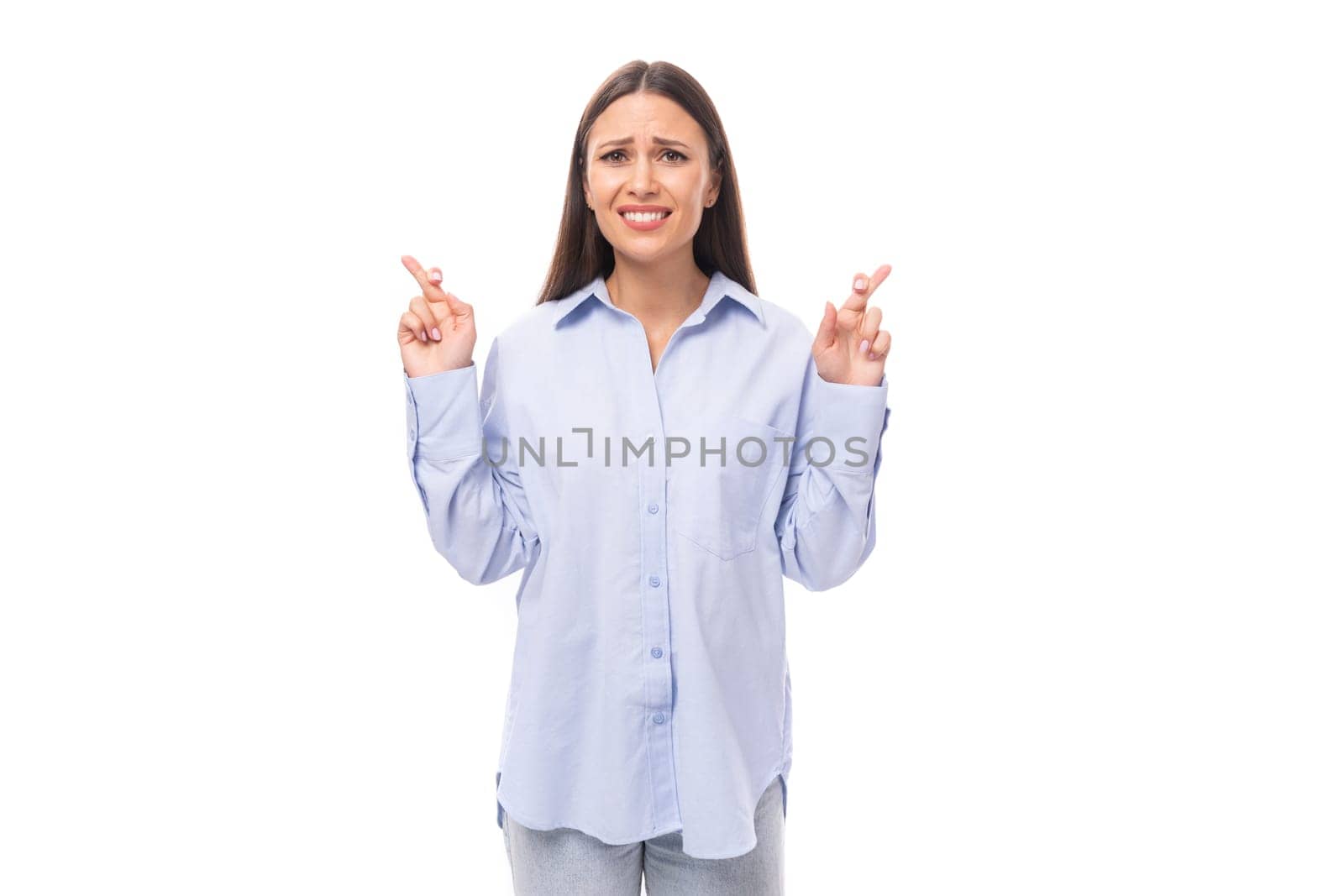 pretty young brunette european woman dressed in a blue shirt shows with her hands to the place for advertising on an isolated background with copy space.