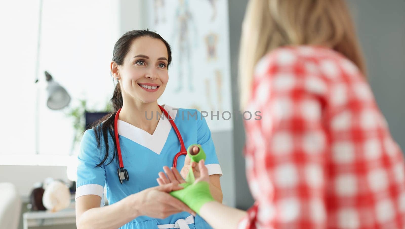 Woman traumatologist bandaging injured arm of young female patient in clinic. First aid for trauma surgical treatment of wounds concept