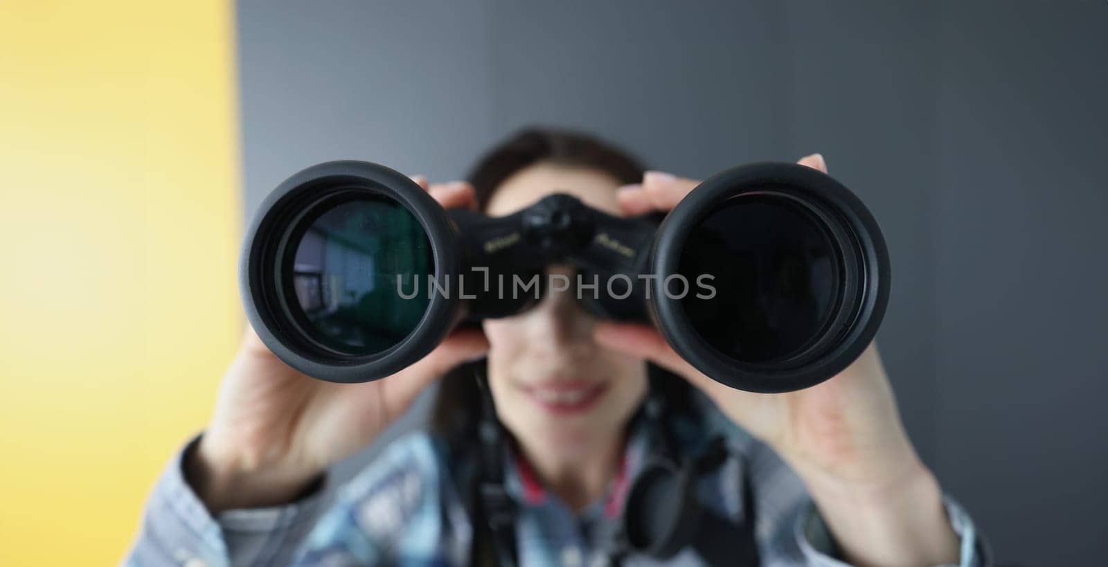 Young woman looking through black professional binoculars closeup. Baby tracking mobile apps concept