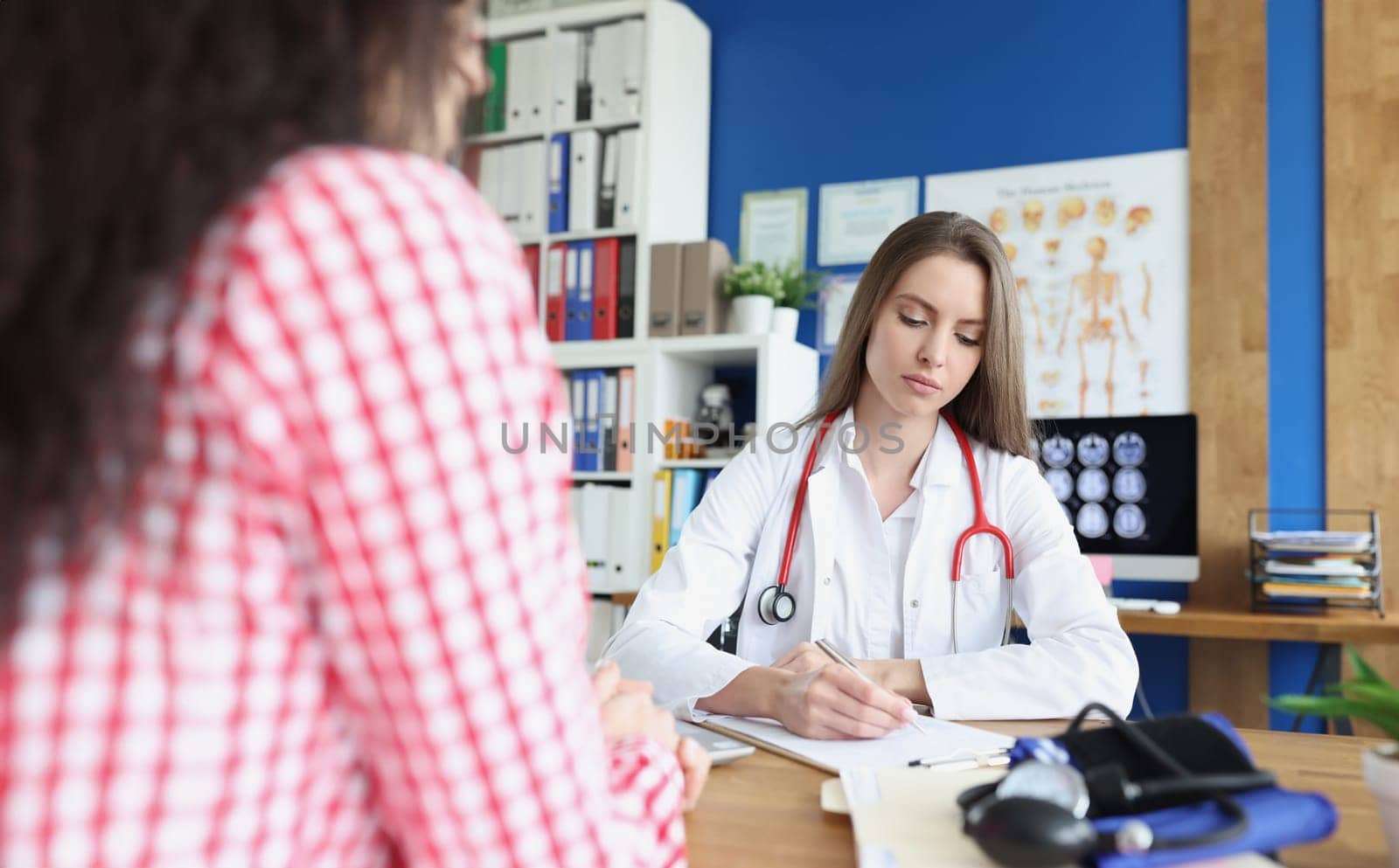 Doctor writing in documents next to female patient in clinic. Health care concept