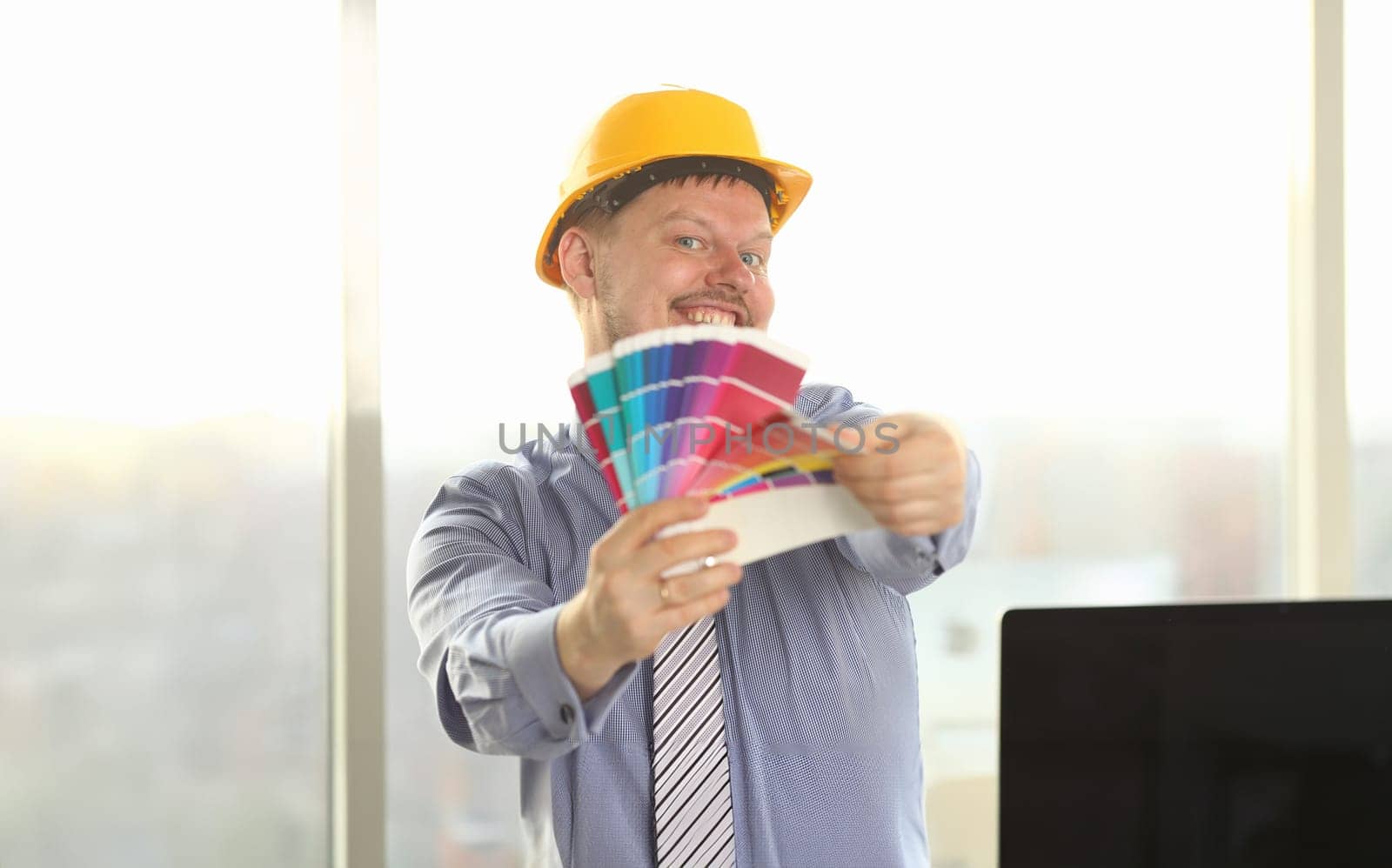 Portrait of Happy Male Designer Hold Color Palette. Architecture Draft Tools Colour Swatches for Selection. Freelance Joyful Foreman in Yellow Protective Helmet Posing with Paint Swatch