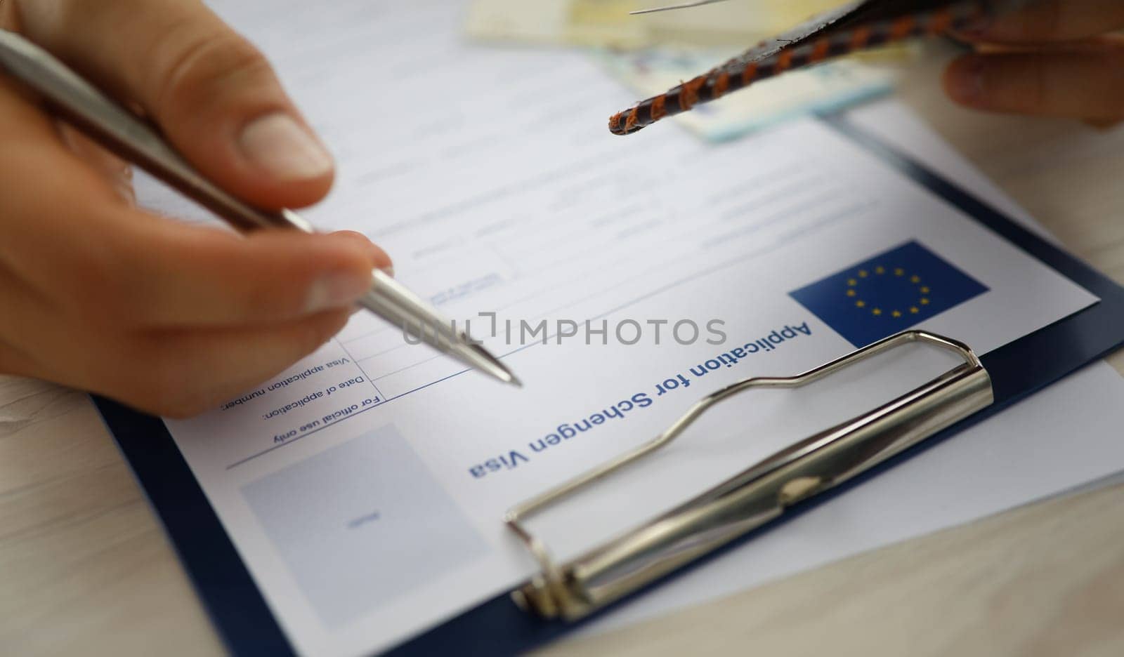 Close-up of male person filling application form for schengen visa holding silver pen. Writing personal information on paper. Travelling abroad or immigration concept