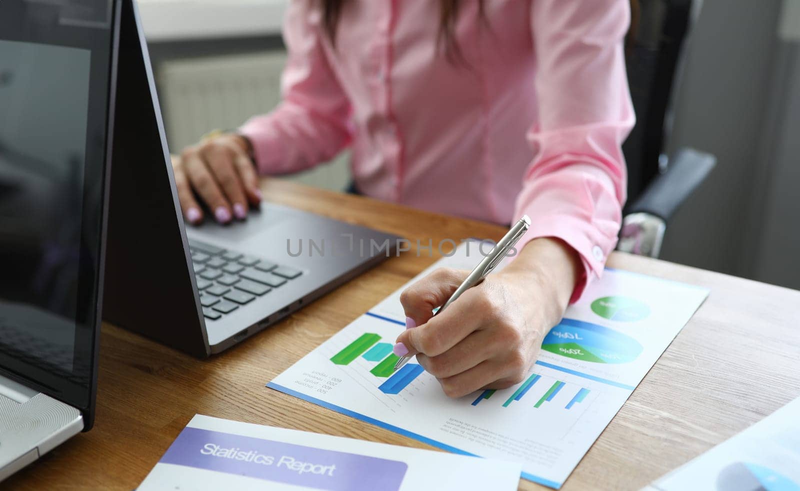 Close-up of professional office worker prepare statistics report for company. Woman working on black computer. Papers with diagrams on desktop. Business and economy concept