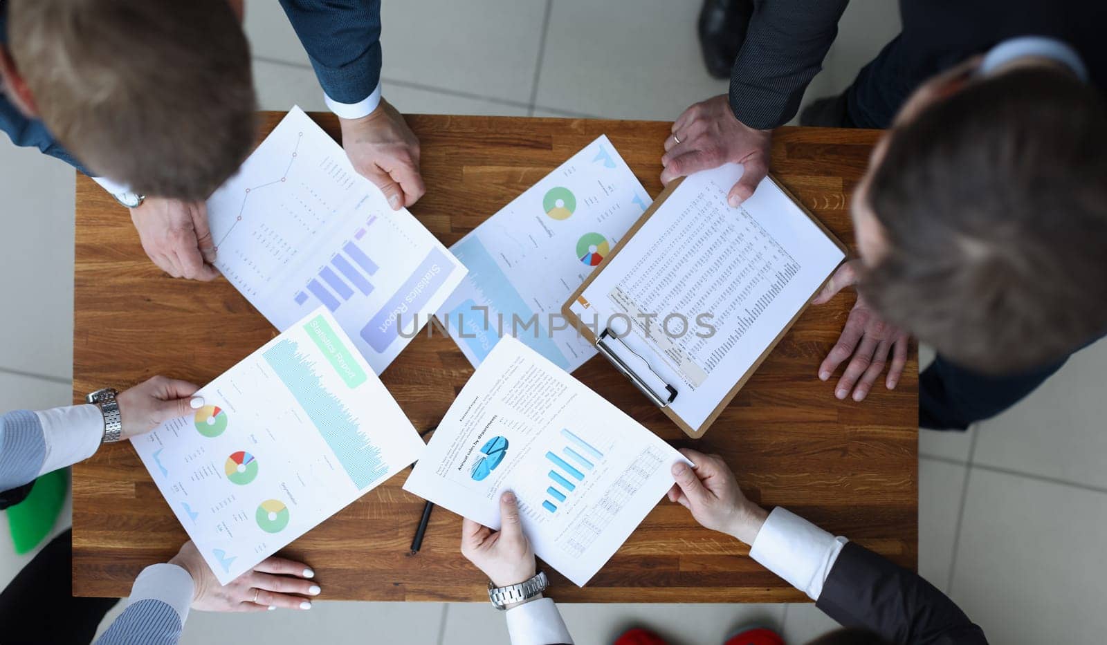 Top view of smart business people discuss important question in office. Papers with charts and diagrams. Stylish wooden table. Business and conference room concept