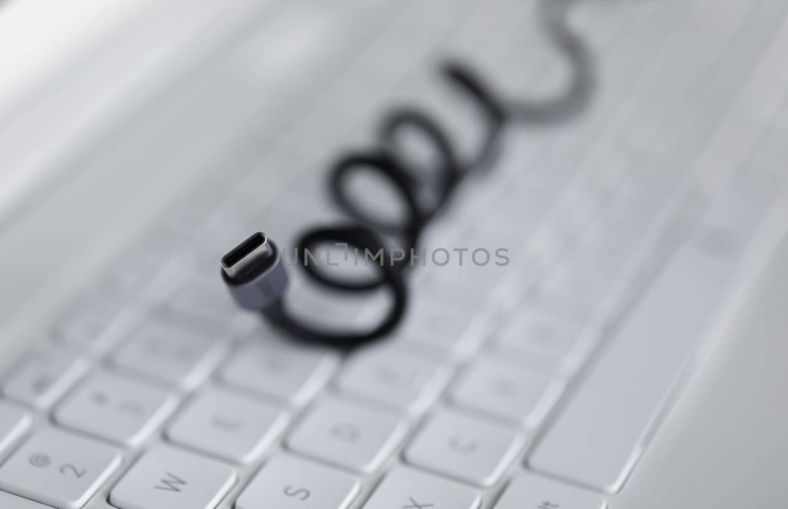 Close-up of black cable for connecting to device lies on white computer keyboard. Laptop accessories. Usb input for tablet. Fast charger. Modern technology and pc concept