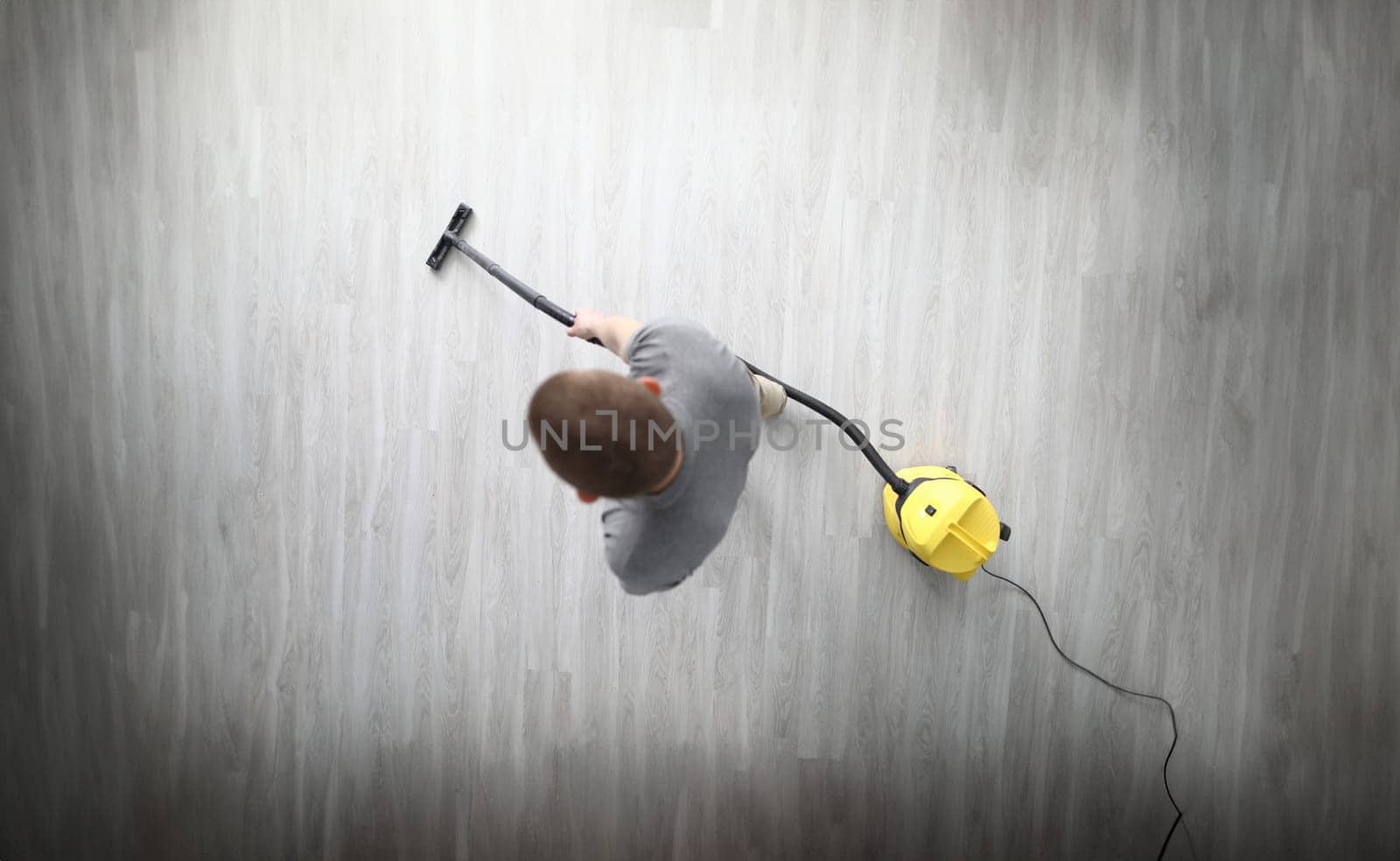 Top view of adult male cleaning in room with compact yellow vacuum cleaner. Grey laminate floor in modern flat. Technology. Renovation and cleaning service concept