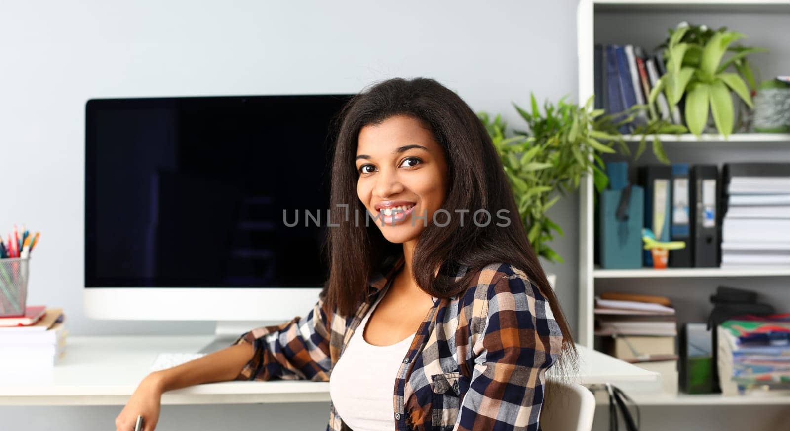 Black smiling woman sitting at workplace looking at camera portrait