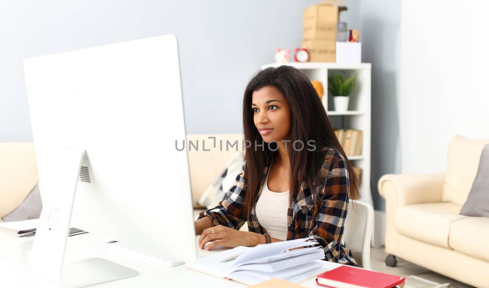 Black smiling woman sitting at workplace working with desktop pc studying or doing school homework concept