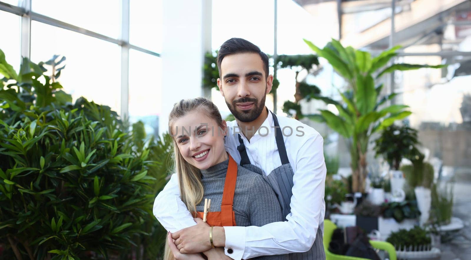 Smiling Man Hugging Woman in Home Plant Center. Female and Male Gardener Standing in Store with Green Domestic Flower and Trees. People Standing in Botanic Shop Looking at Camera Photography