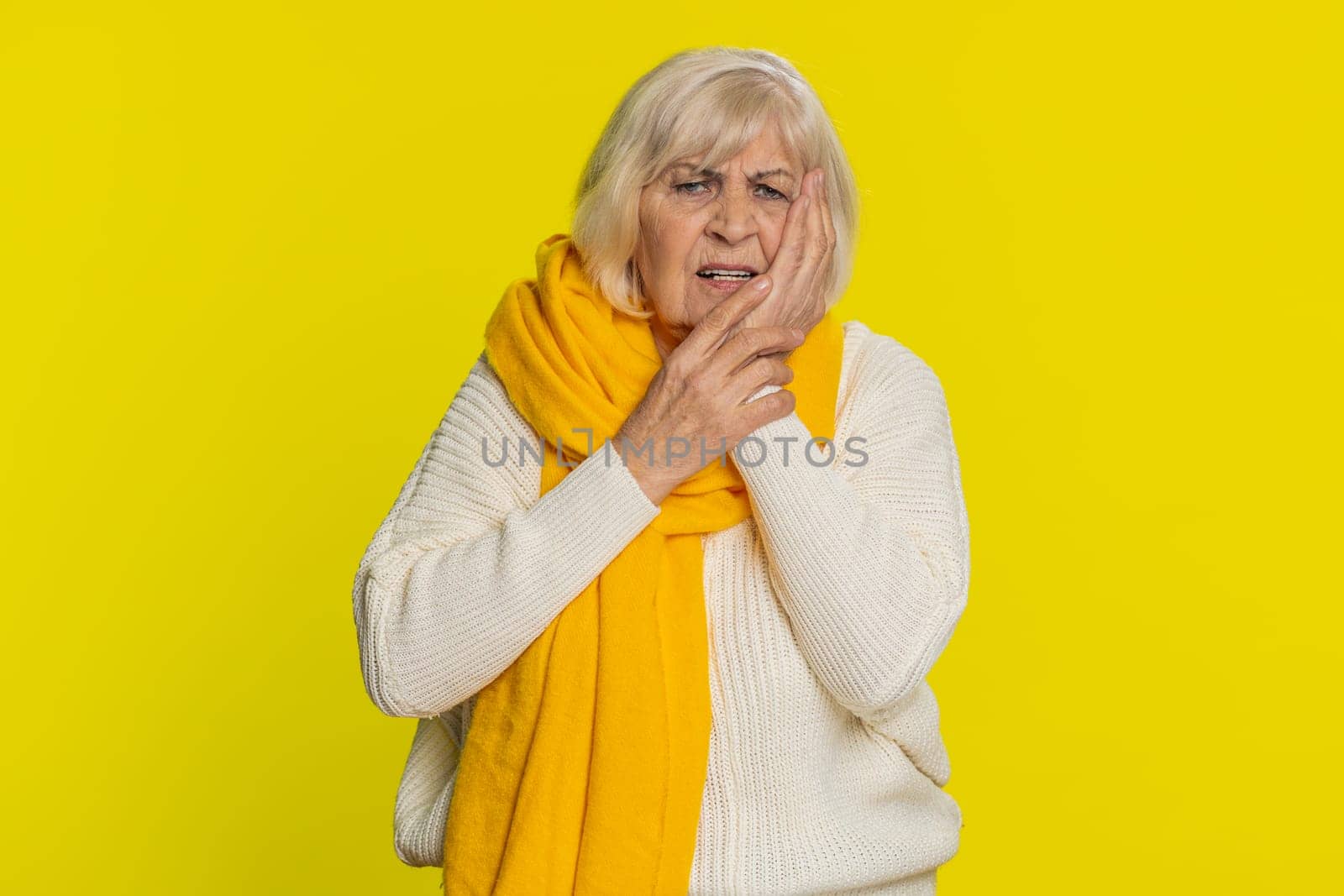 Dental problems. Senior old woman touching cheek, closing eyes with expression of terrible suffer from painful toothache, sensitive teeth, cavities. Mature grandmother pensioner on yellow background