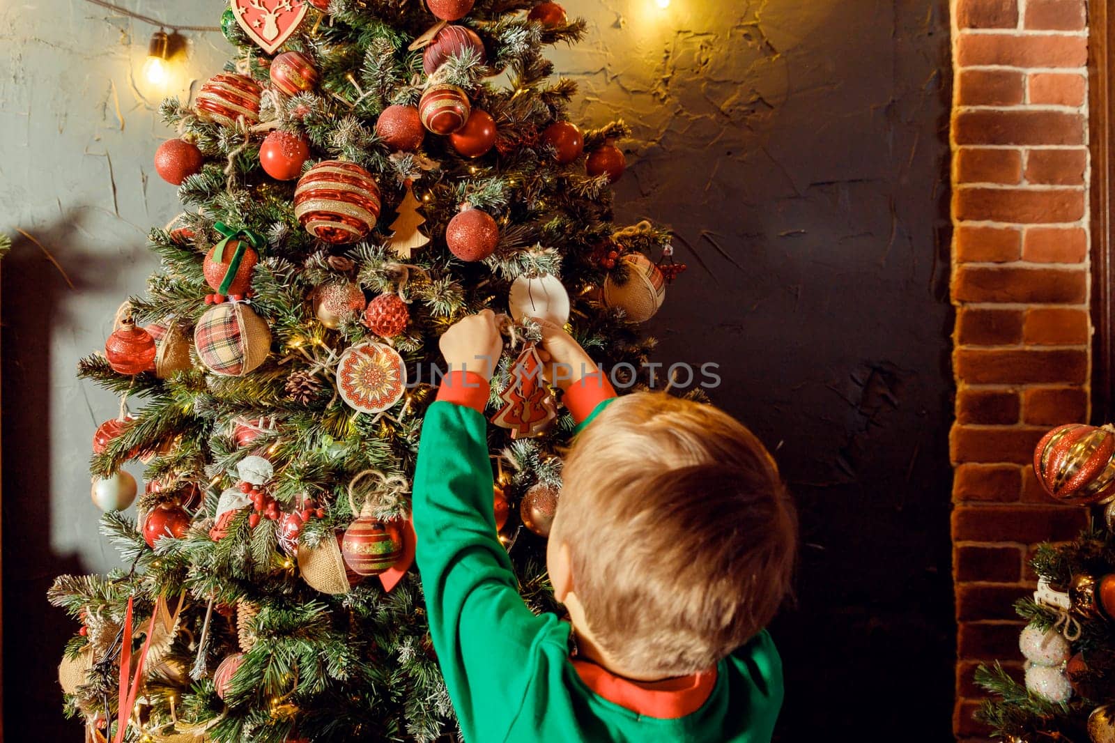 Child hanging a Christmas boot decoration illuminated on a Christmas tree from colorful ambient glowing lights.