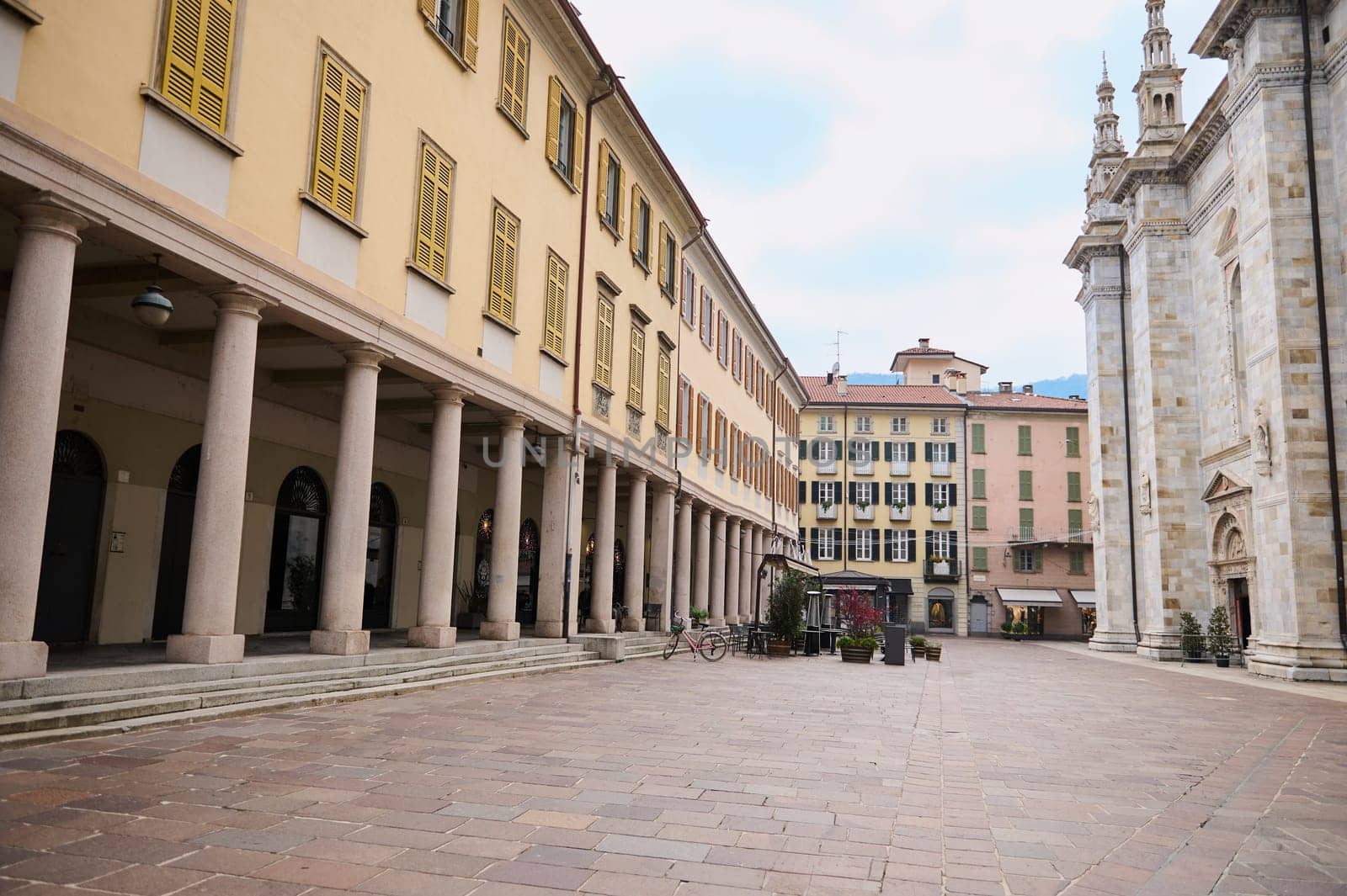 Como, Lombardy, Italy. Photography of empty street in in the center of Italian city of Como, with columns near the entrance of medieval cathedral of Santa Maria Maggiore. Beautiful architecture