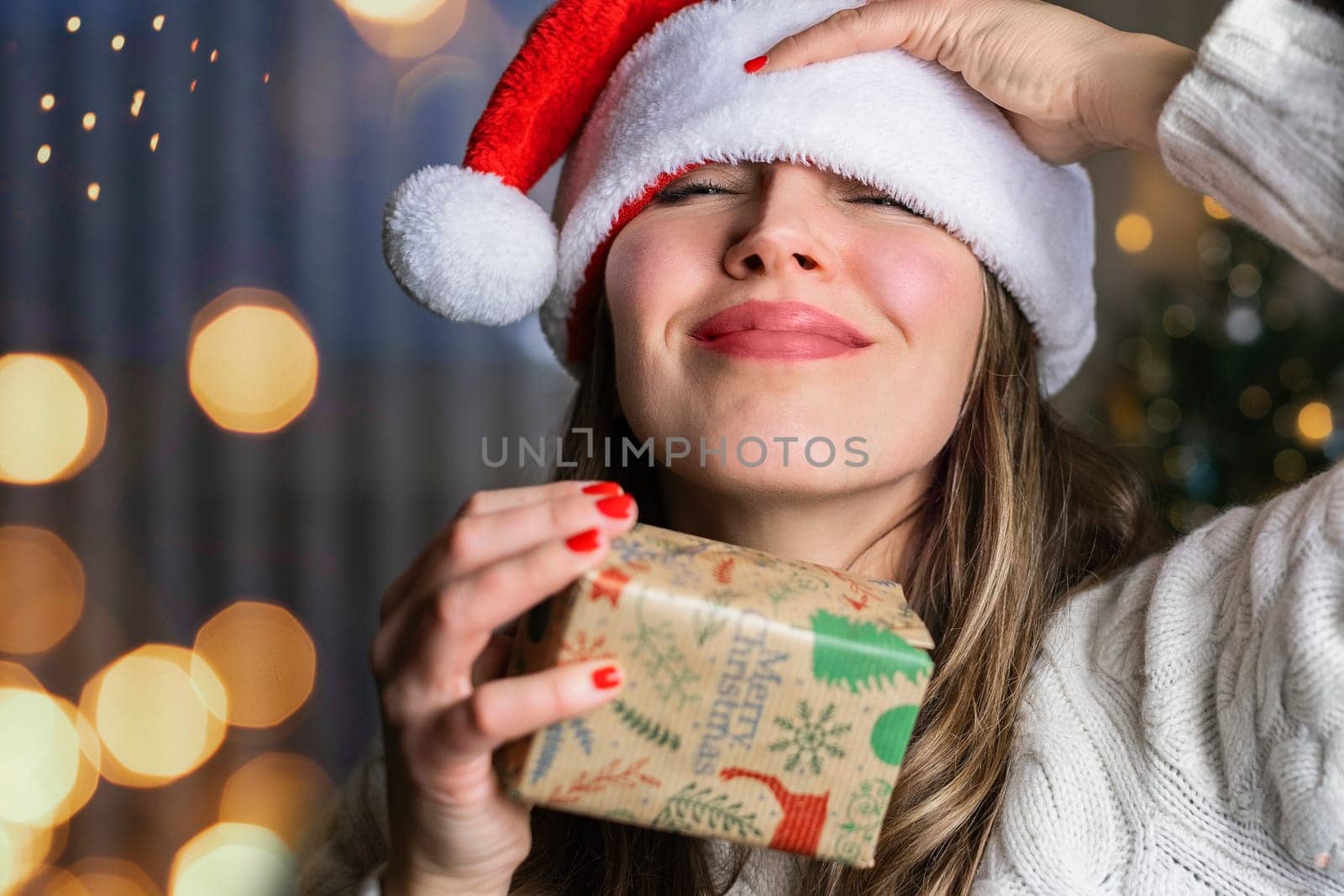 Smiling Woman in Santa hat with new year gift in background of lights.