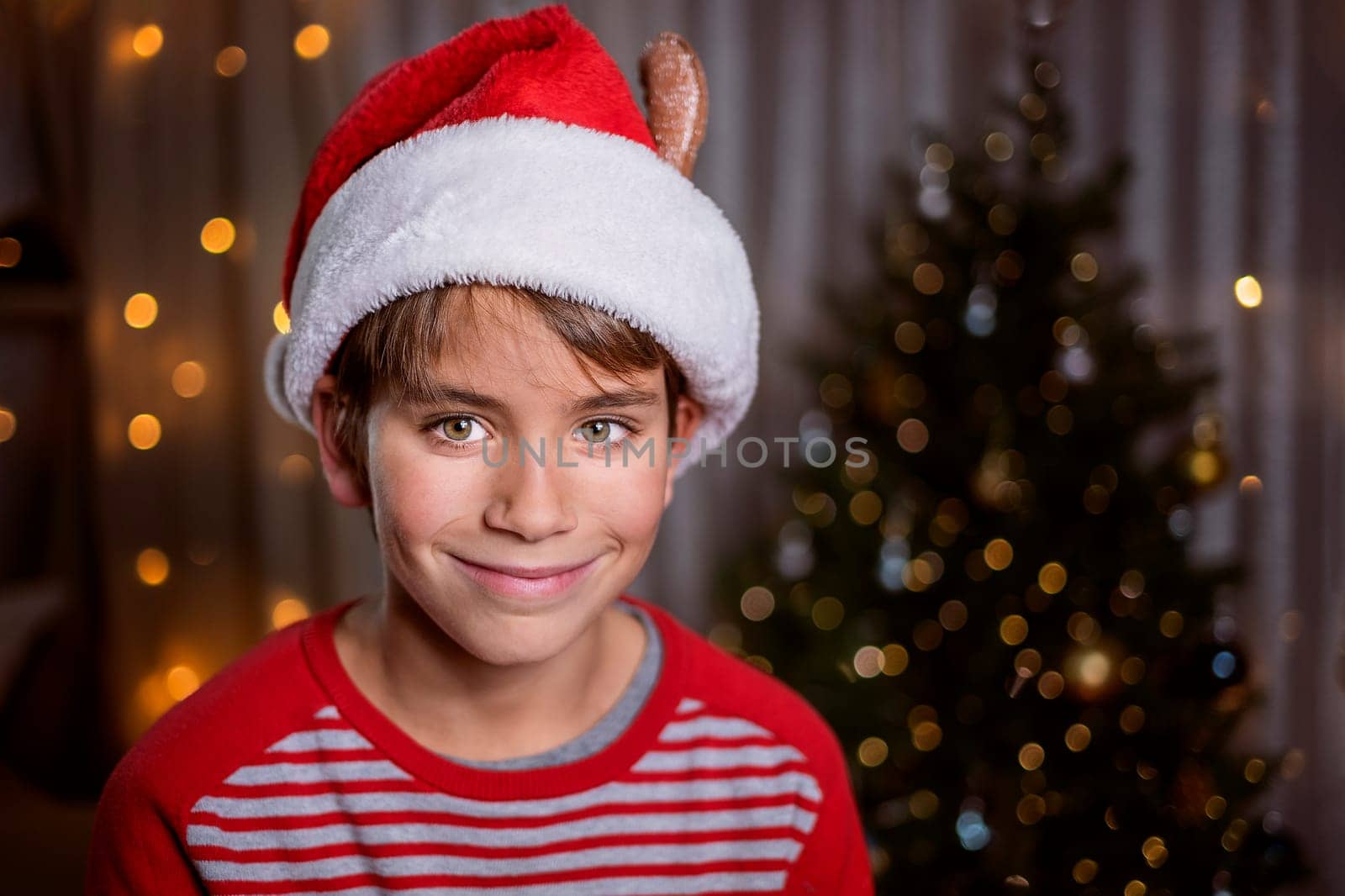 Smiling boy in Santa red hat on Christmas tree background and lights. Christmas concept