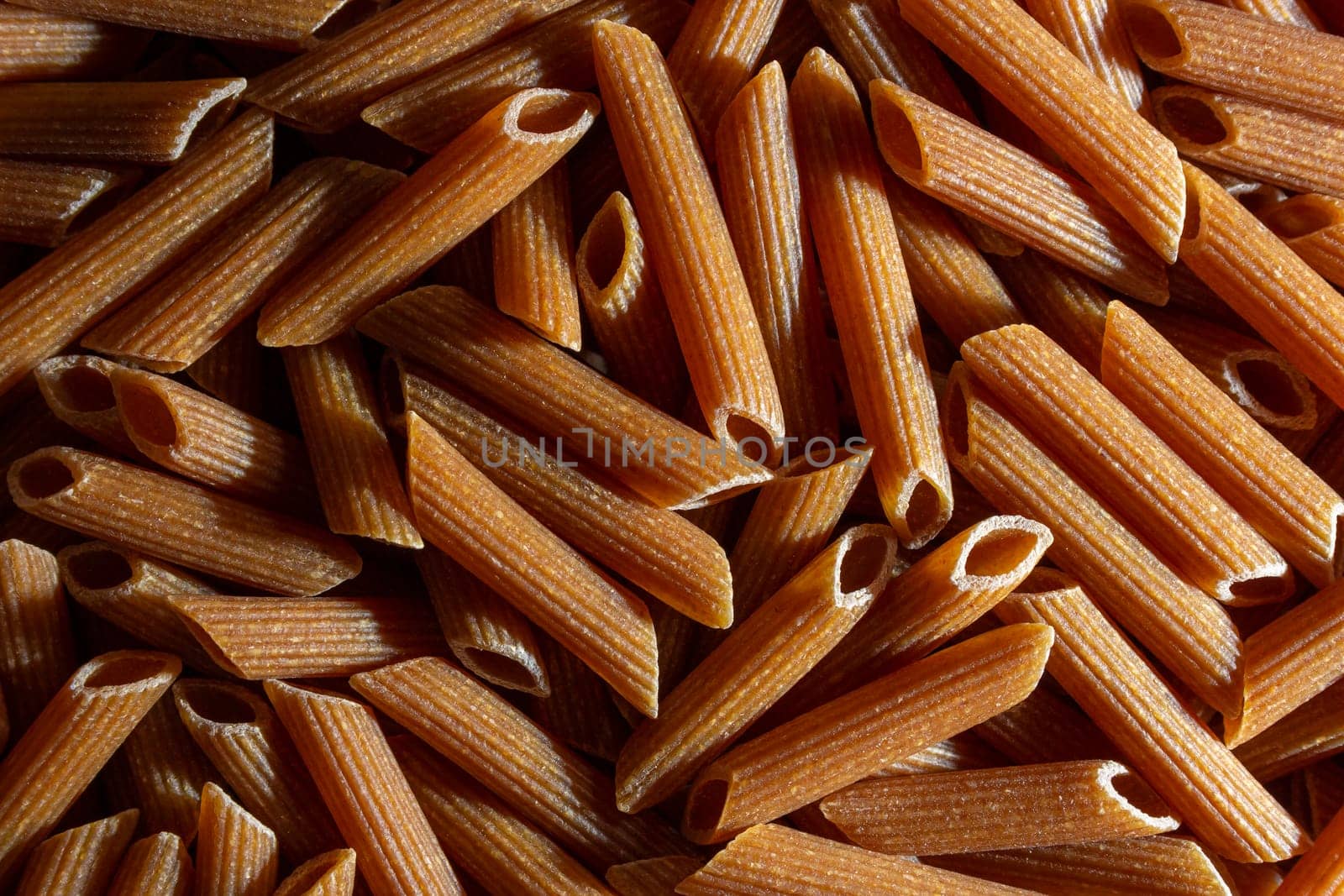 Uncooked Whole Grain Penne Rigate Pasta Background by InfinitumProdux