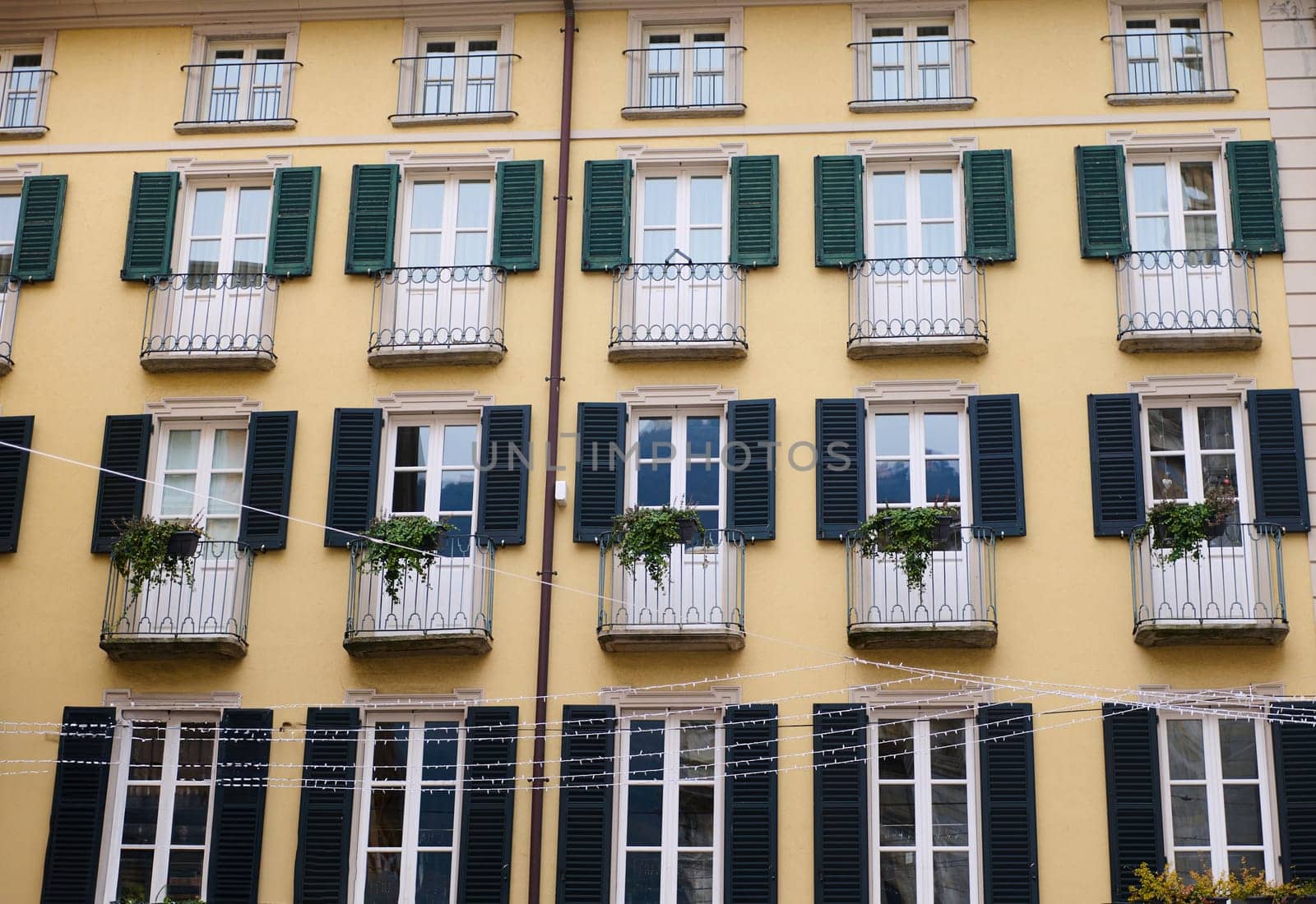 Italian architecture. The facades of a house with beautiful balconies decorated with flowers and plants in the city center of Italian Como in Lombardy