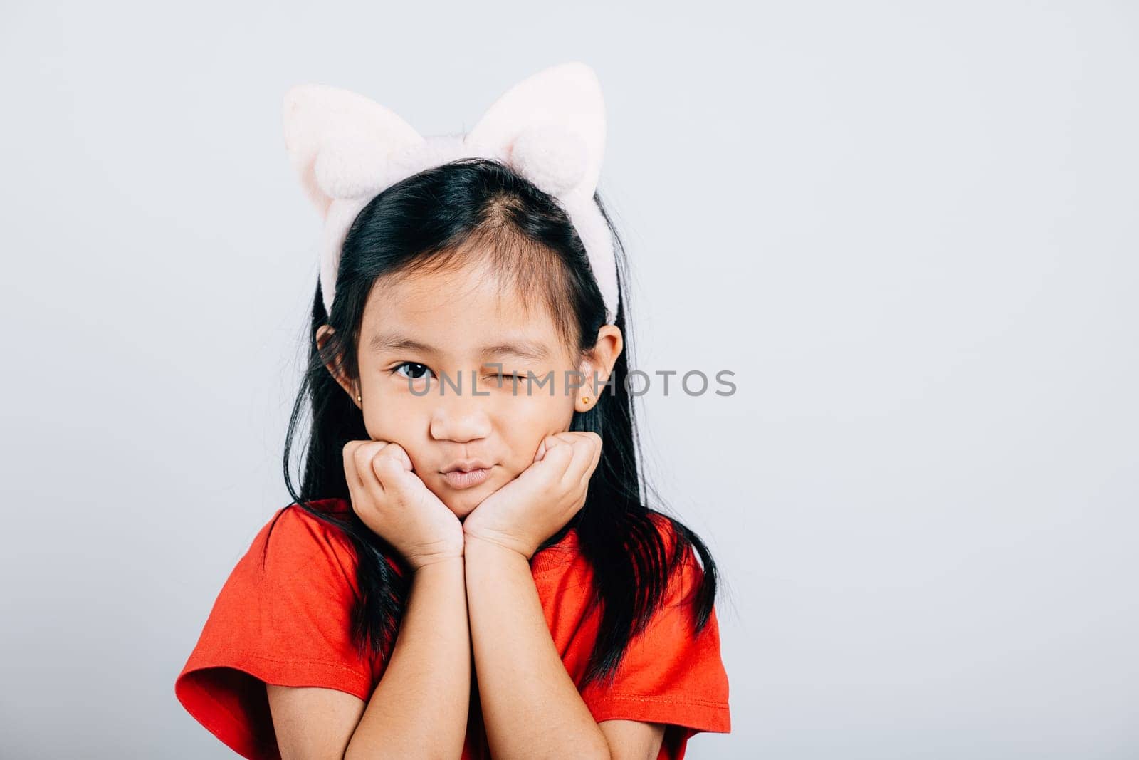 A joyful Asian kid girl in a red t-shirt beams with happiness her open mouth revealing a big smile and confidence. Isolated portrait of a cheerful child on a white background. by Sorapop