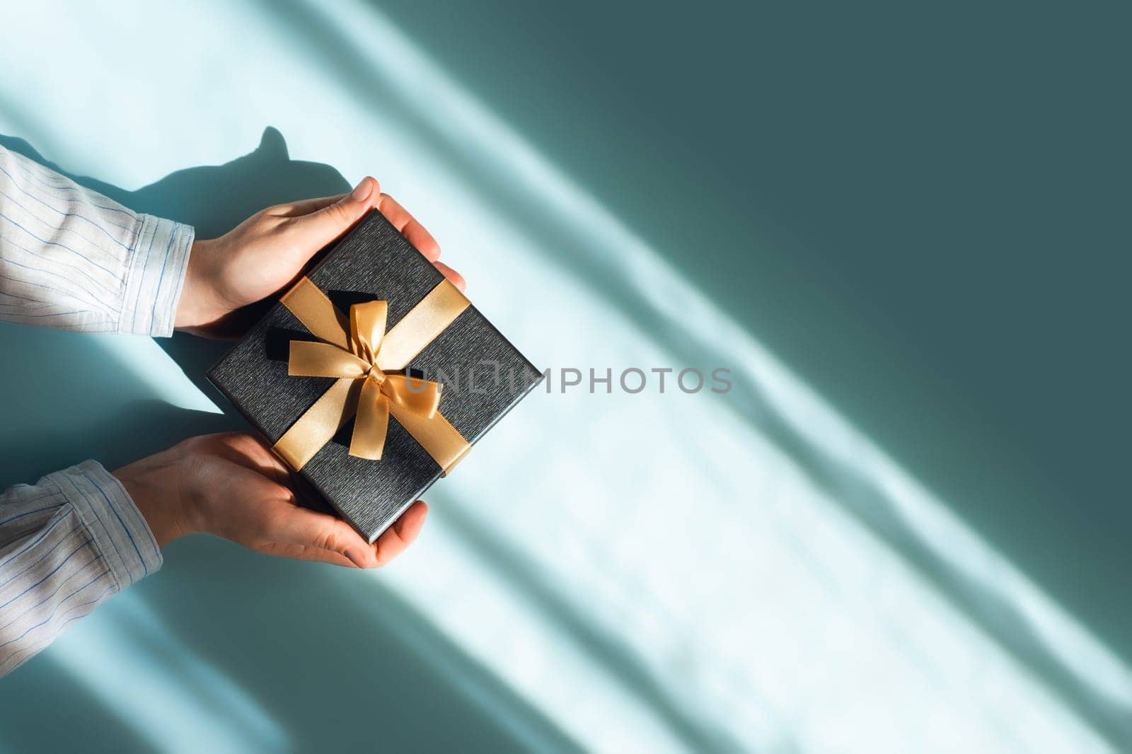 Flat lay with gift box in a female hands on sunlights on blue background. Top view, place for text.