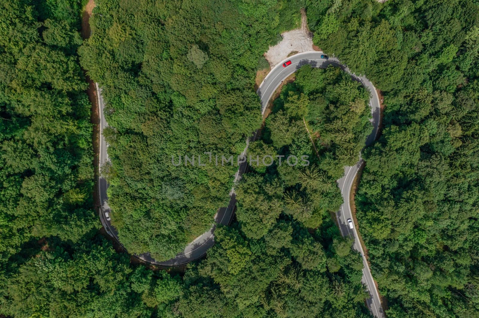 Aerial view of a red car driving along a serpentine road through a green forest