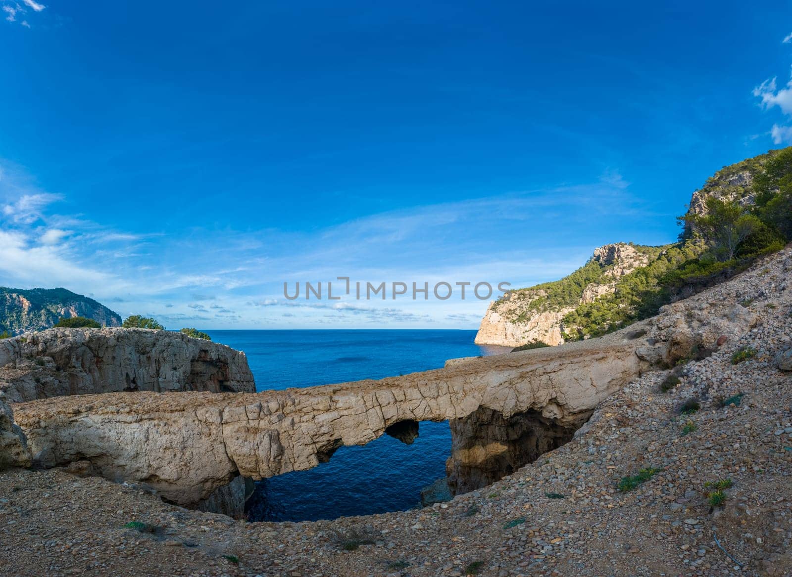 Impressive rock arch on Ibiza's coast, contrasting with blue sky and turquoise sea.