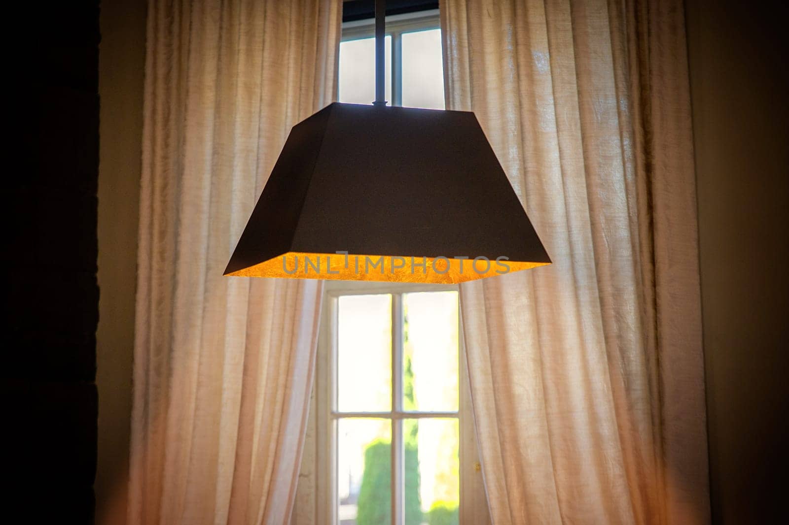 A lamp hanging from the ceiling shines with warm light in front of a window with curtains by Rom4ek