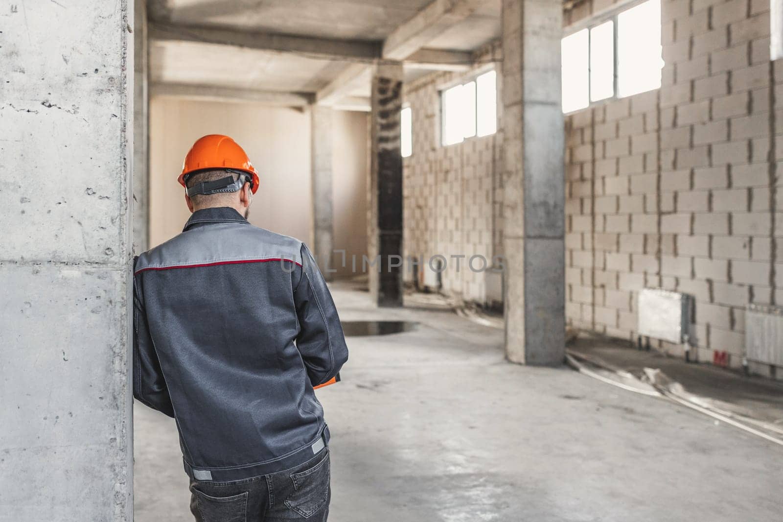 A construction worker in a helmet stands with his back to the camera, leaning on a reinforced concrete structure, thinking about something, copy space.