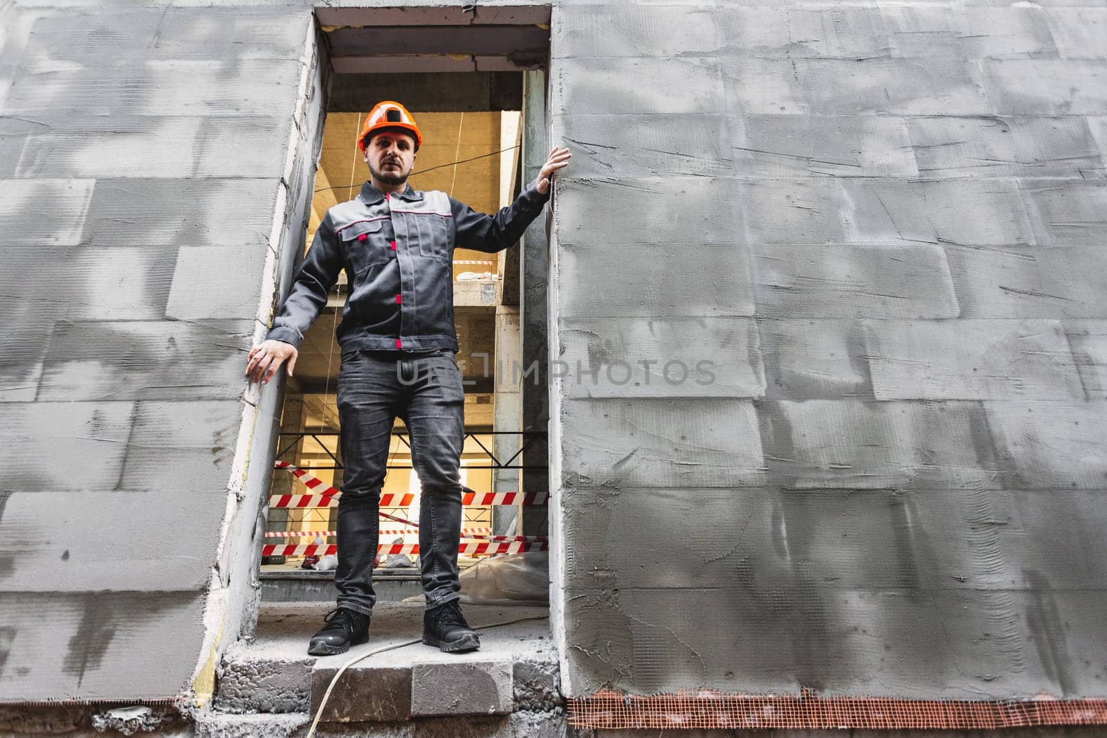 A construction worker in overalls stands in the opening of a building under construction, copy space by Rom4ek