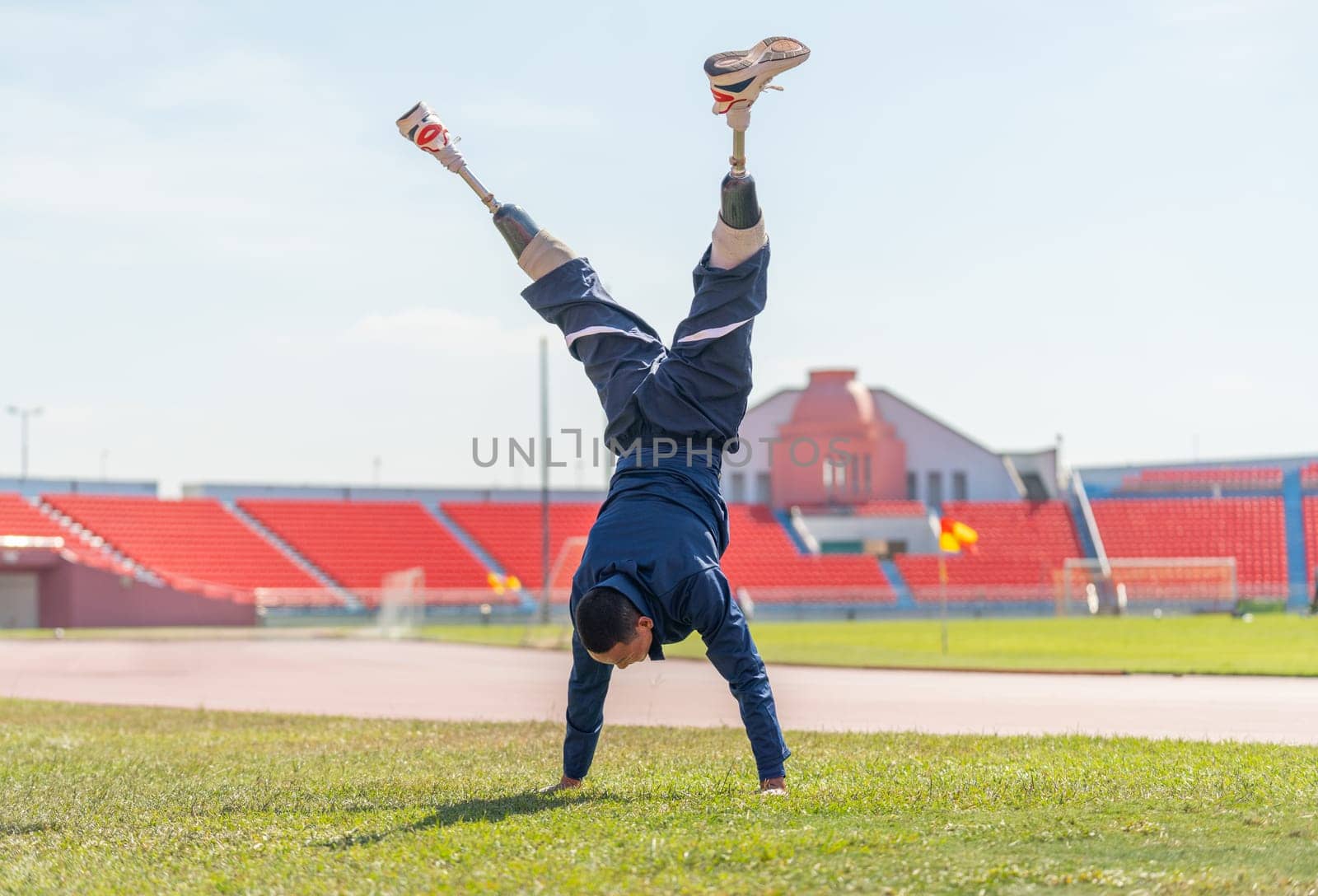 Sport man athlete with a prosthesis on his leg warm up the body with do the handstand in area of grass field in the stadium with day light.