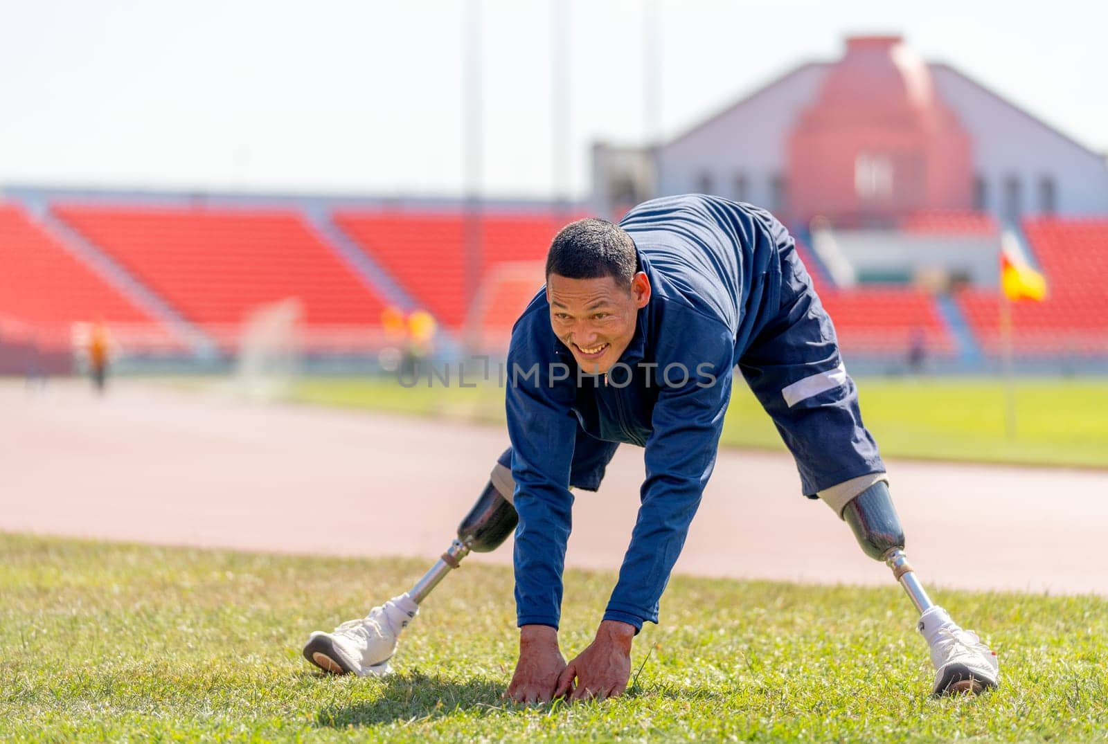 Sport man athlete with a prosthesis on his leg action of warm-up the body by spread his leg and bend body forward in area of grass field at the stadium, sport concept.