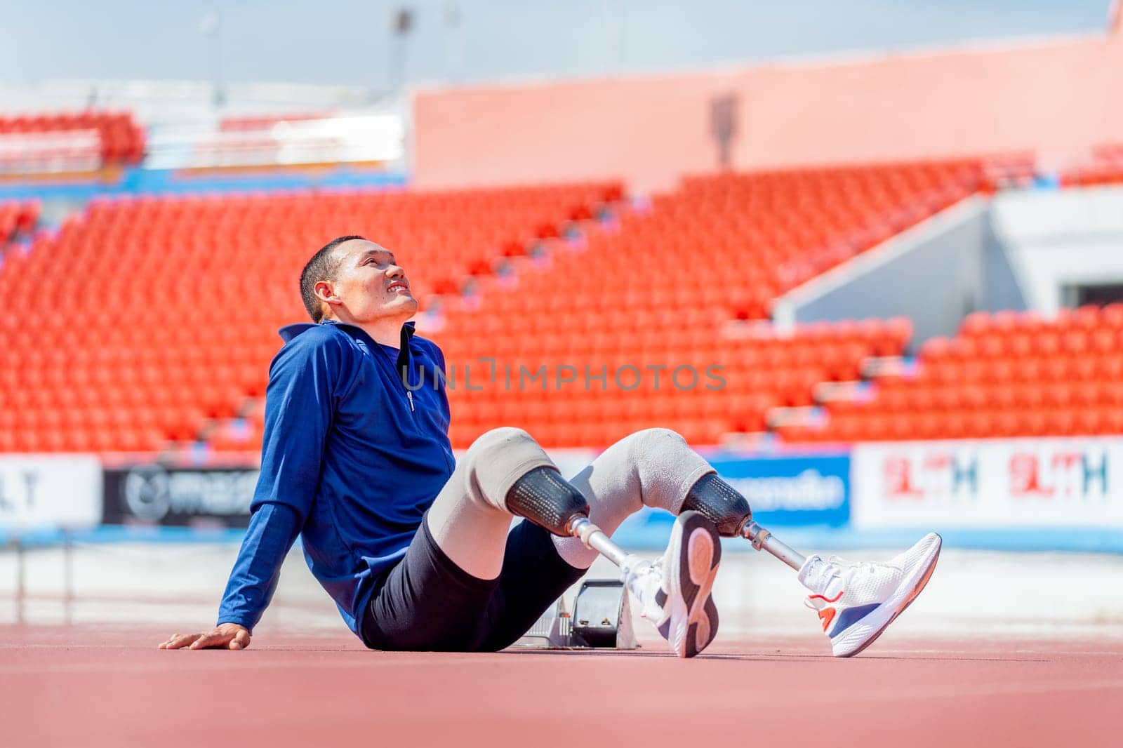 Sport man athlete prosthesis legs sit on the track and look over at the stadium to relax after exercise with happiness.