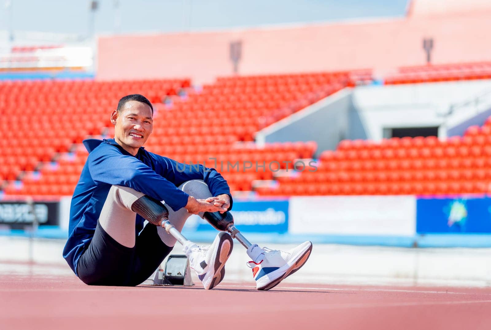 Sport man athlete prosthesis legs sit on the track and look at camera with smiling after exercise at the stadium. Sport concept.