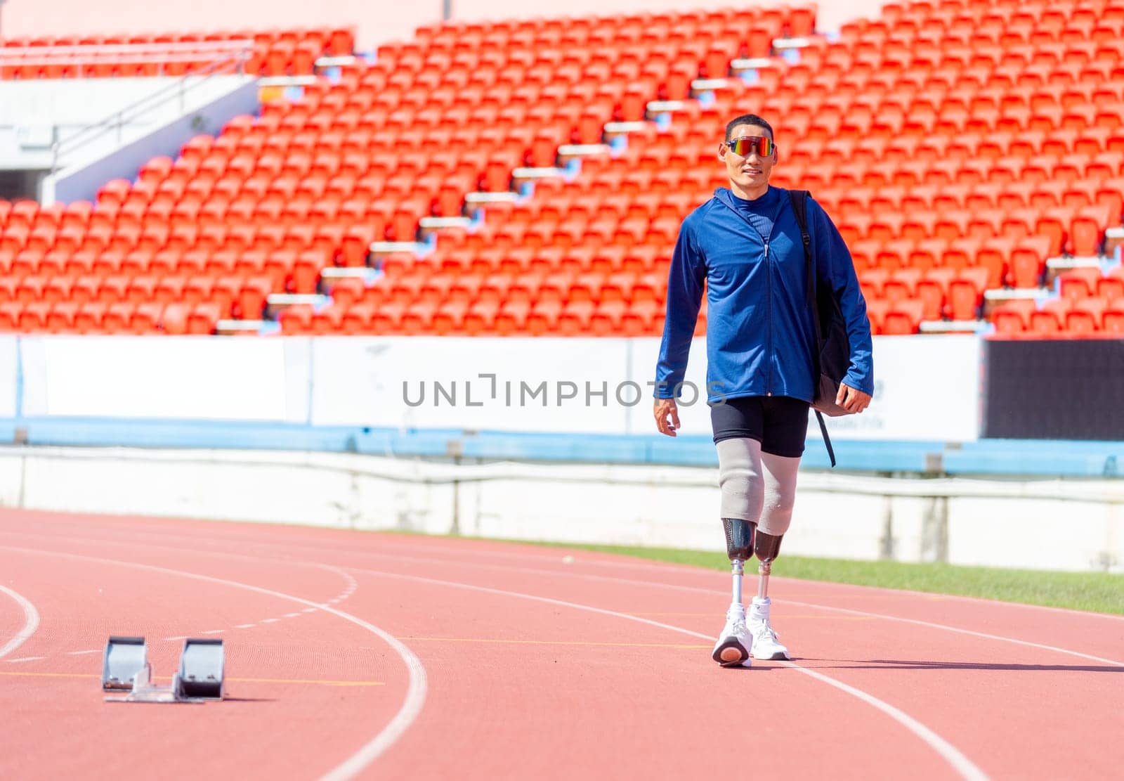 Sport man athlete prosthesis legs with sun glasses carry the bag and walk on the track of the stadium with day light.