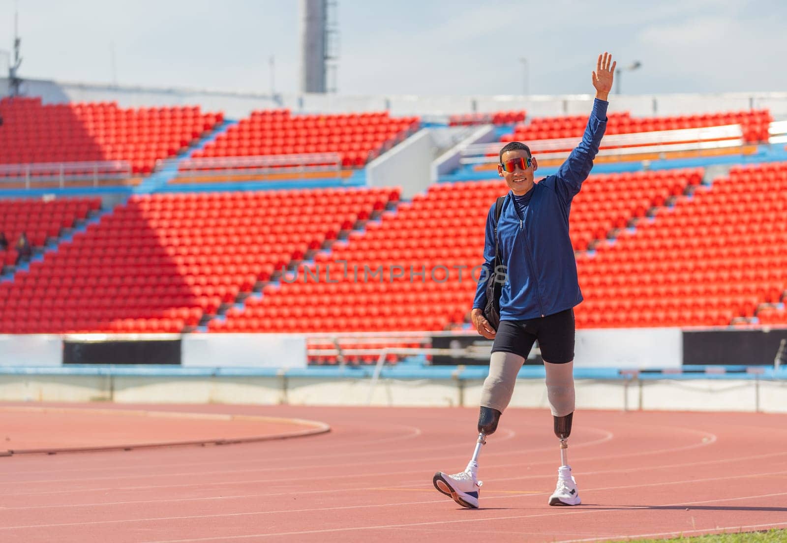 Sport man athlete prosthesis legs carry the bag and walk on the track of the stadium also action of greeting by raise his hands up with happiness.