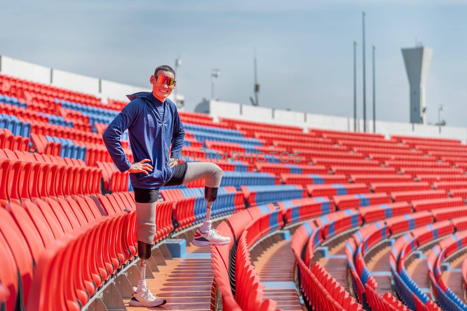 Sport man athlete prosthesis legs stand with put one leg on chair of amphitheater also look at camera in the stadium with smiling.