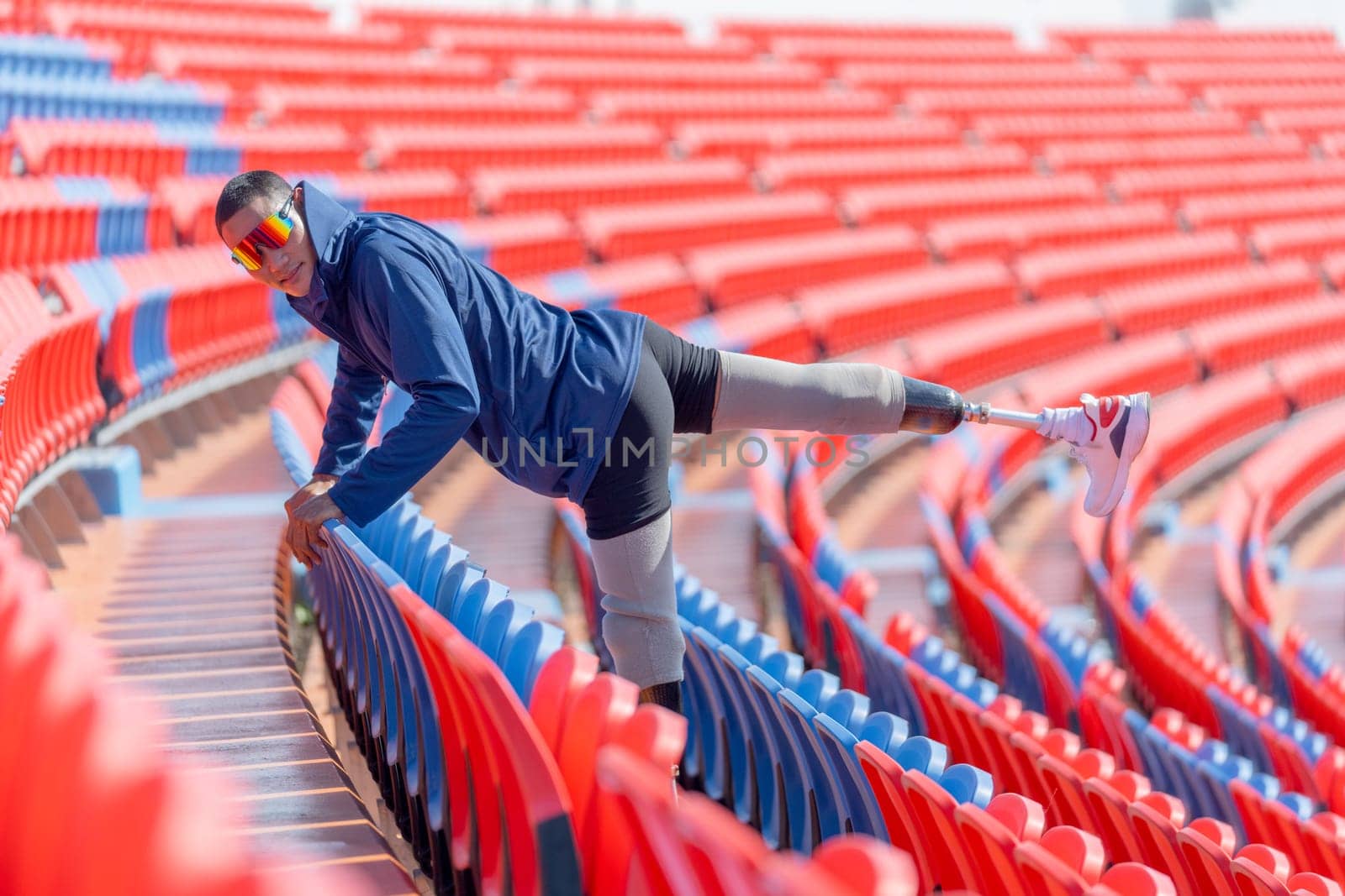 Sport man athlete prosthesis legs use chair of amphitheater to warm up before exercise by raise his leg up and point to the back in the stadium with day light.